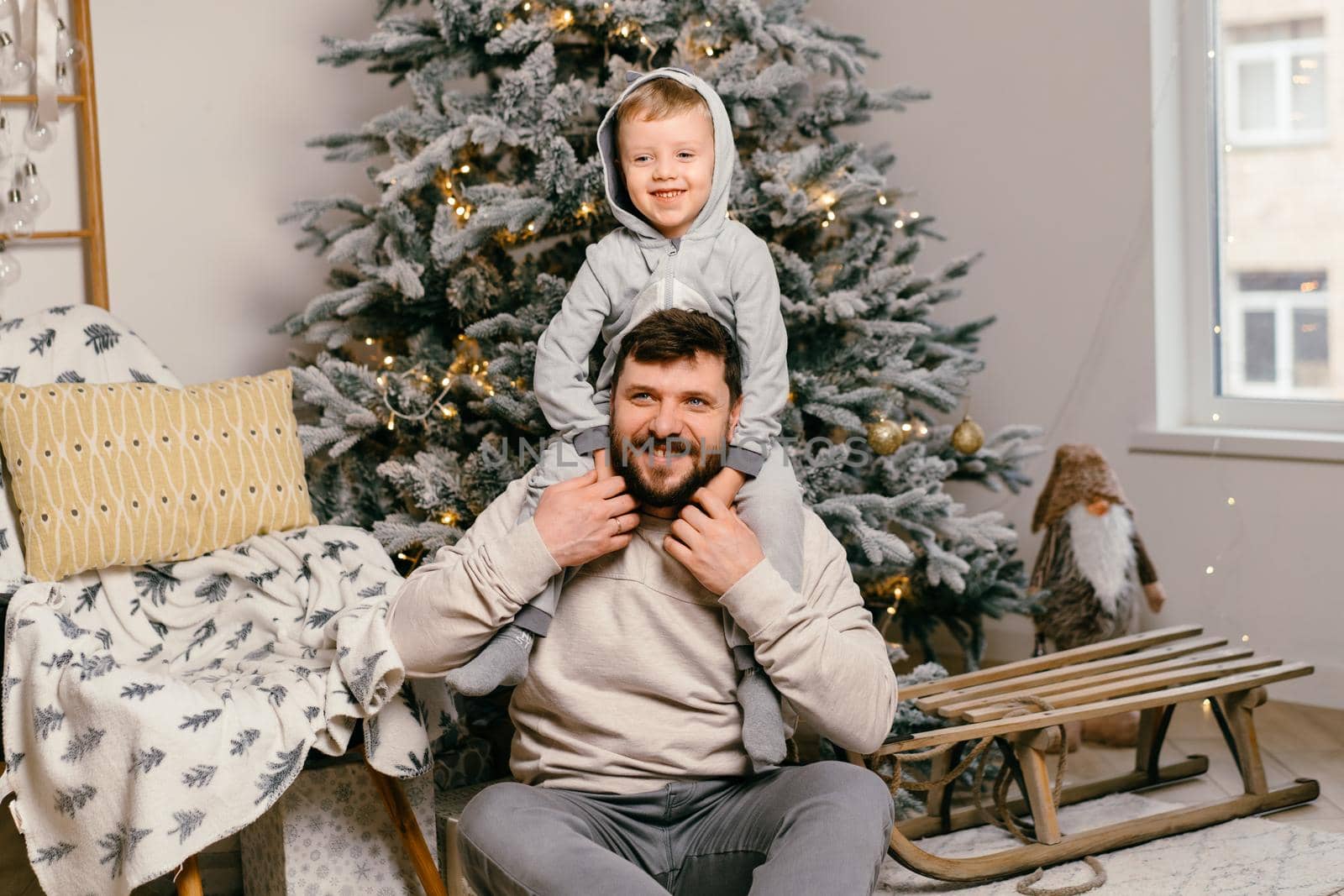 Holiday Christmas Handsome father playing with small cute son near decorated New year tree at home by andreonegin