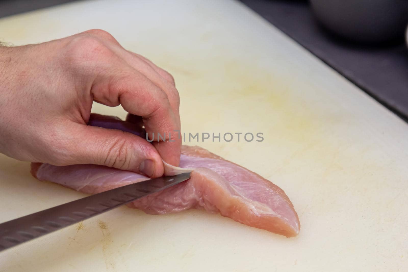 The cook cuts a chicken breast with a knife on a white board.