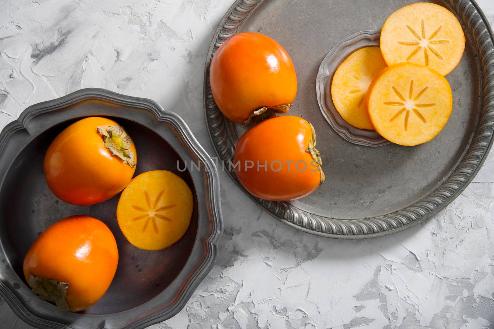 still life with persimmon on a gray cement background in a pewter dish, by KaterinaDalemans