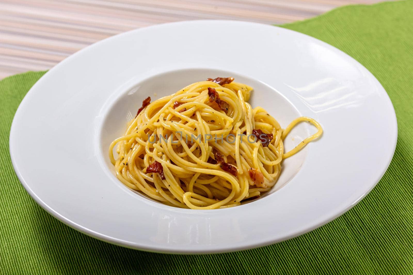 Italian delicious spaghetti carbonara pasta with bacon parmesan cheese garlic creamy sauce lies in a dark wooden round plate, bottle of olive oil, spices and a sprig of green leaves, top view close-up