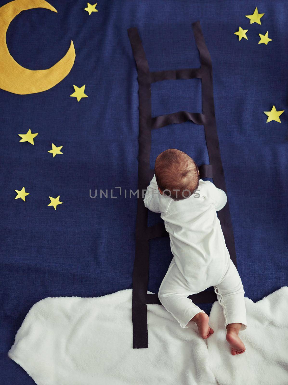 Concept shot of an adorable baby boy climbing a ladder against an imaginary night time background.