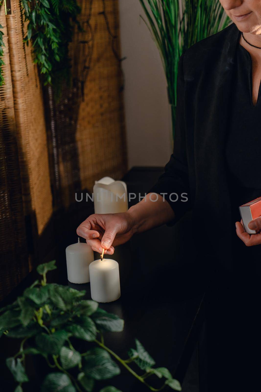 Mature beautician with blonde hair, lighting scented candles with a match for hot wax massage. by CatPhotography