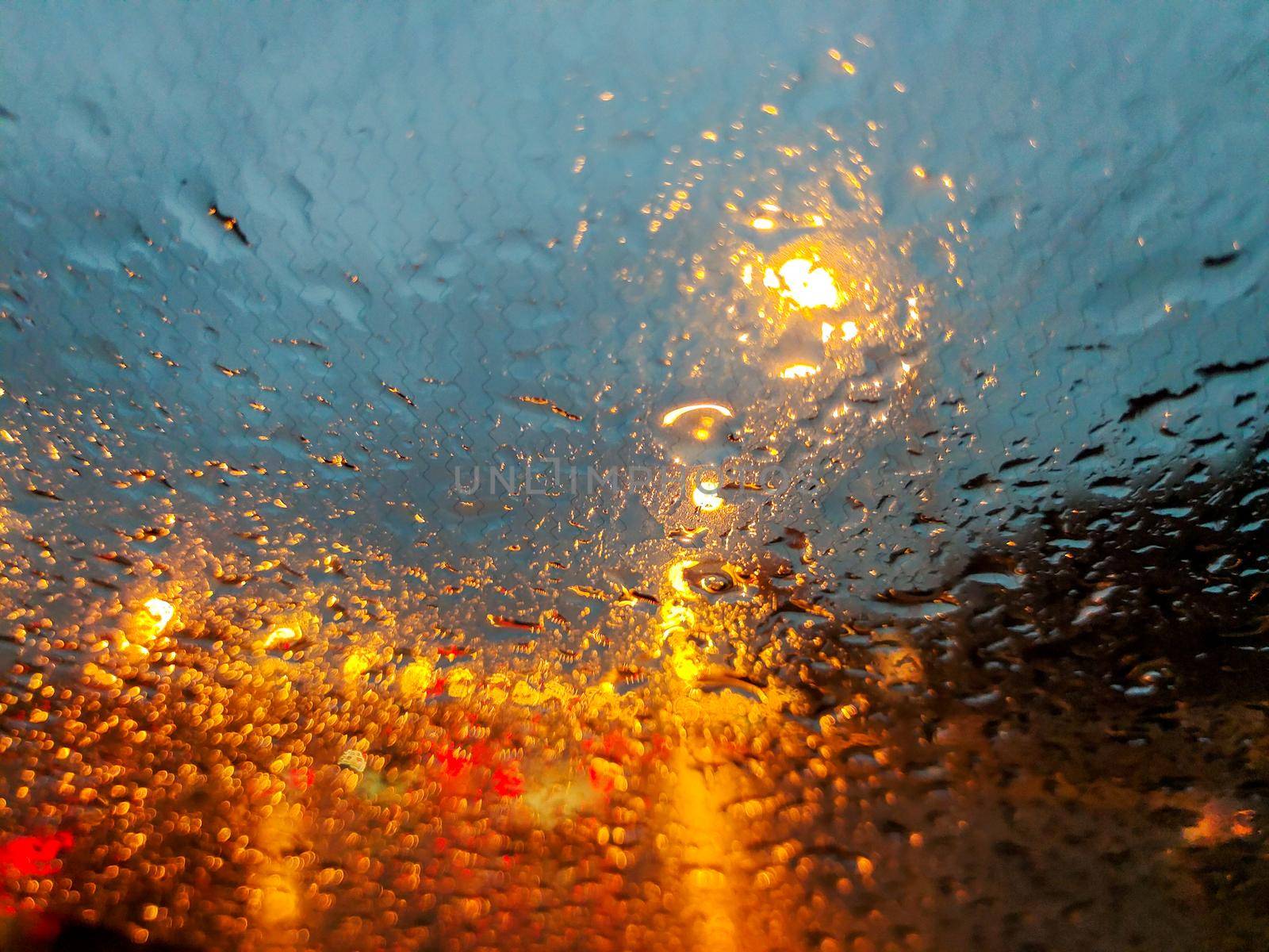 Raindrops on the windshield of the car. There is a lot of traffic, the lights of cars are reflected. by Milanchikov