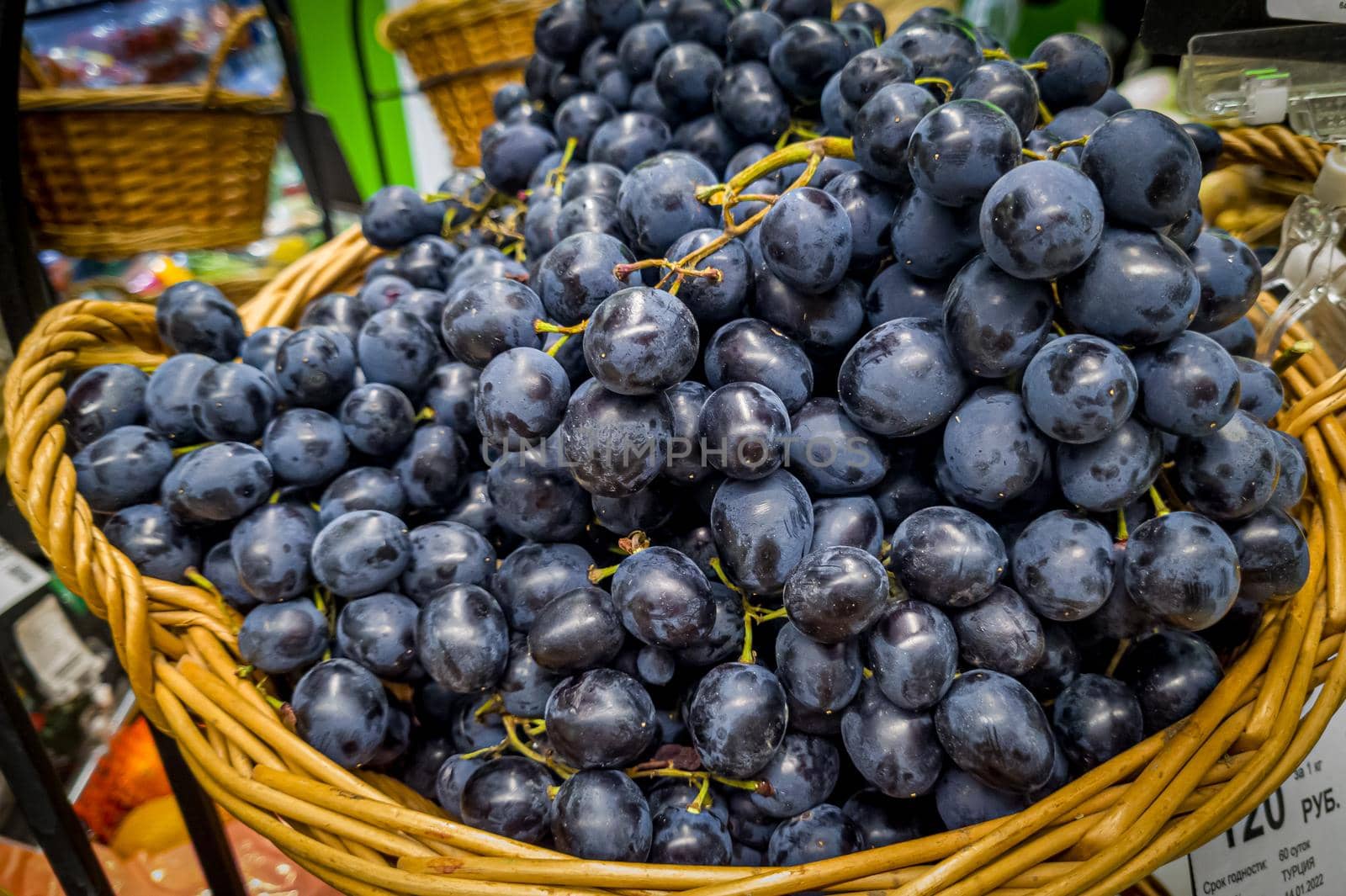 Bunches of blue grapes are in a basket in the store.