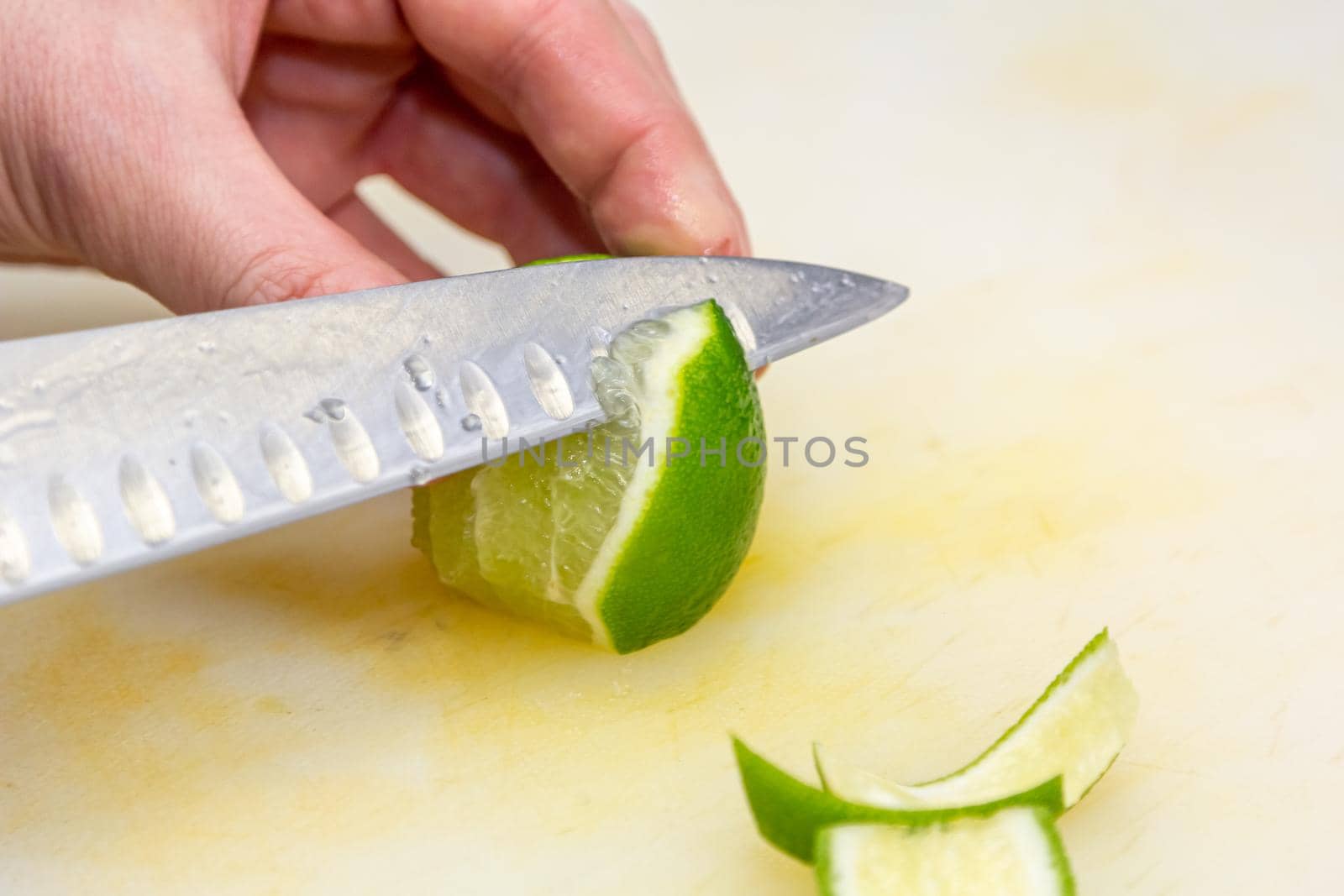 The chef cuts the skin from the lime with a knife on a white board by Milanchikov