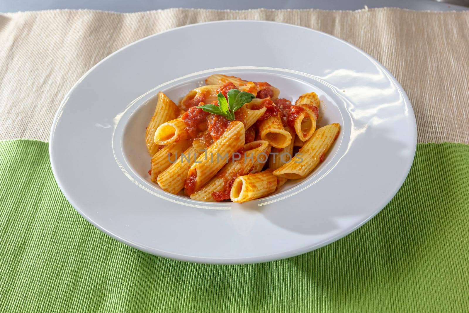 Serving of spicy savory italian penne pasta garnished with fresh basil by Milanchikov