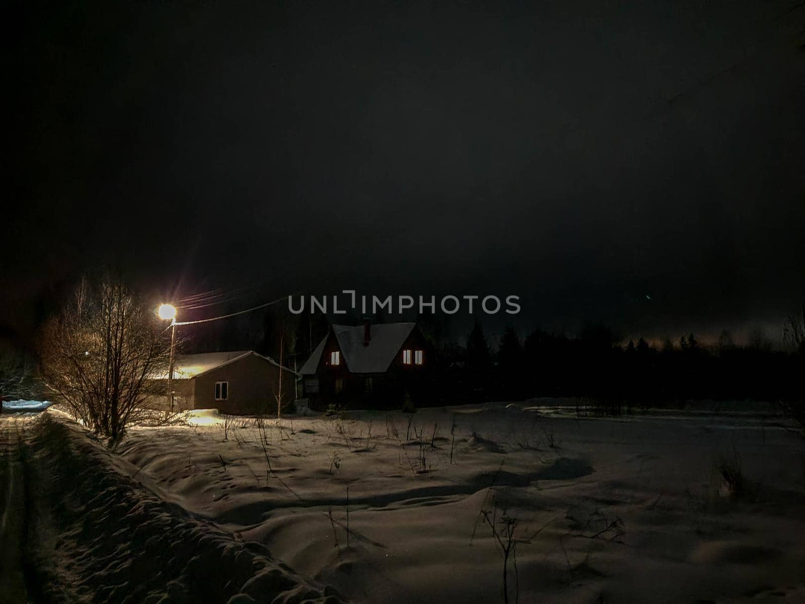 Russian village at night in winter. A road covered with snow and light from the windows of houses