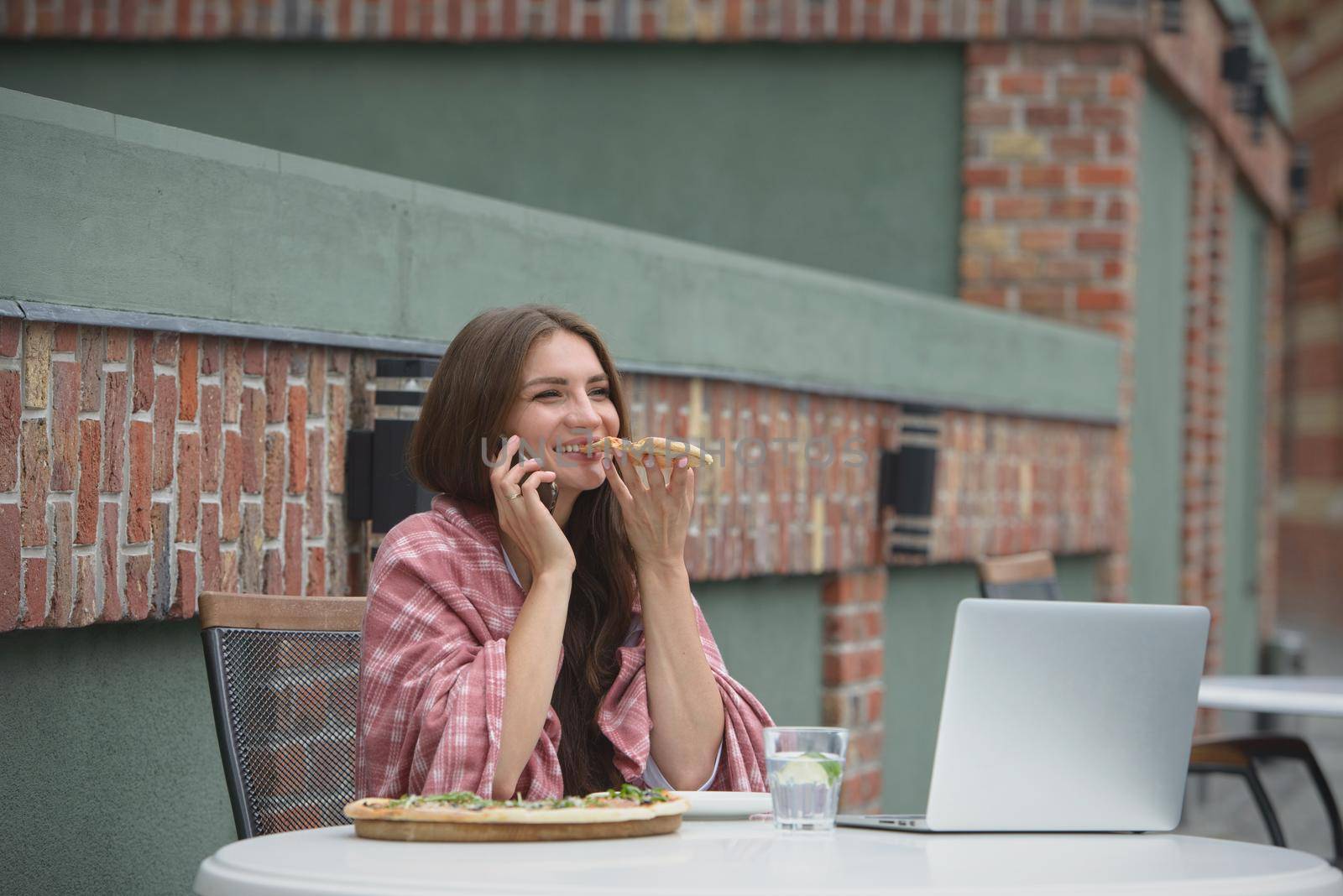 Young freelancer communicates using smartphone while eating pizza in cafe by Ashtray25