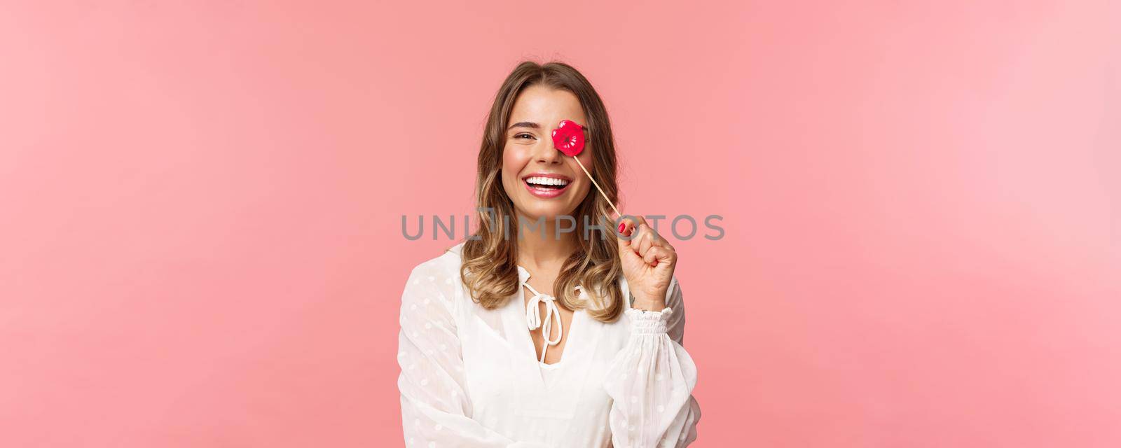 Spring, happiness and celebration concept. Close-up portrait of funny and carefree young beautiful blond girl having fun at party with girlfriends, holding lips stick and laughing, pink background.