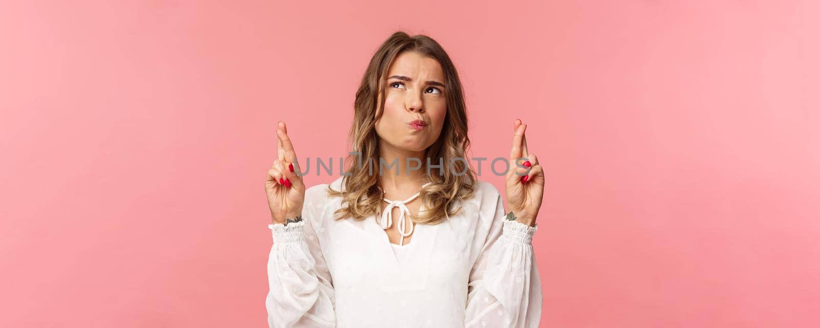 Close-up portrait of hesitant and thoughtful attractive blond girl making assumption, cross fingers good luck, squinting uncertain while thinking and looking up, standing pink background.