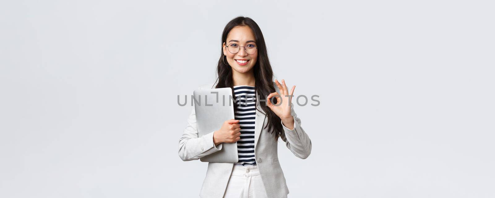 Business, finance and employment, female successful entrepreneurs concept. Young confident businesswoman in glasses, showing okay gesture, hold laptop, guarantee best service quality by Benzoix