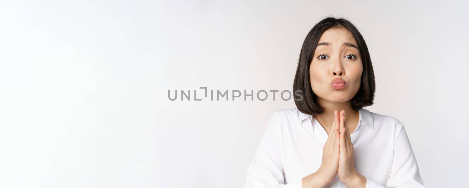 Cute asian woman begging, say please, asking for favour, need help, standing with coy face against white background by Benzoix