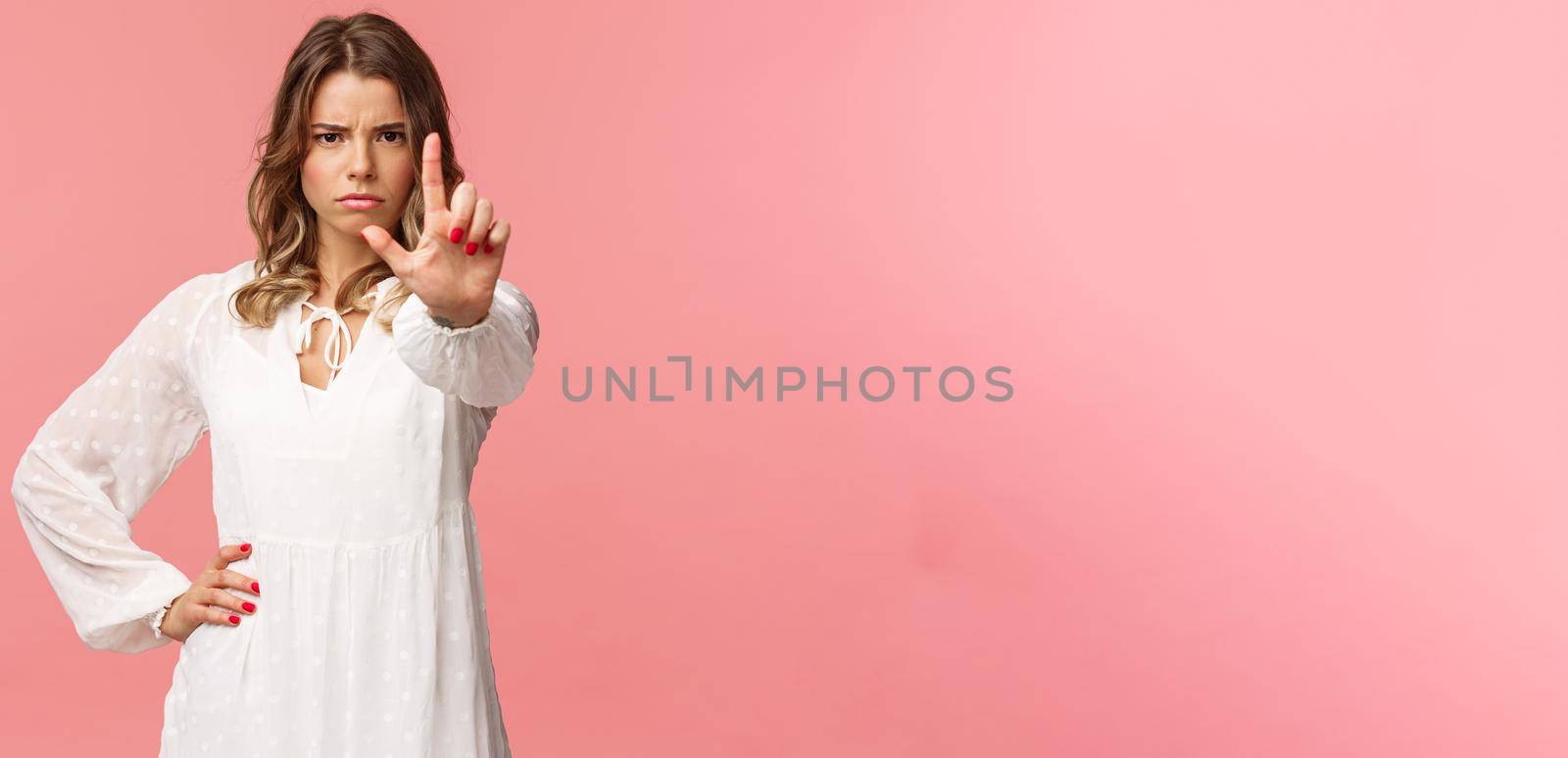 Stop, enough. Portrait of serious-looking assertive and strong blond girl in white dress, extend hand towards camera with one finger raised in warning, frowning angry, forbid and prohibit action by Benzoix