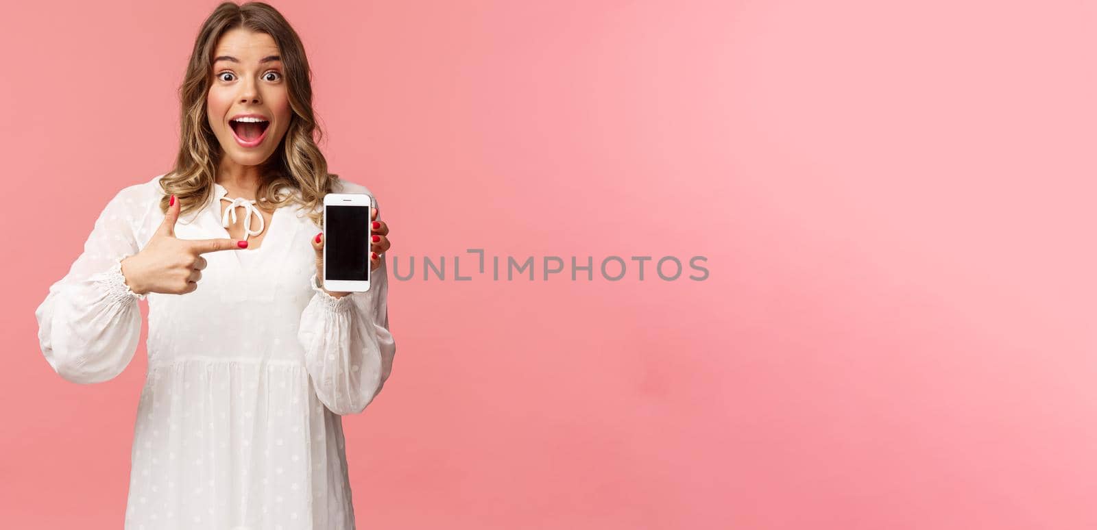 Portrait of impressed, excited young blond woman showing something awesome on display, pointing mobile phone screen and smiling astonished, brag with her recent match on dating app.