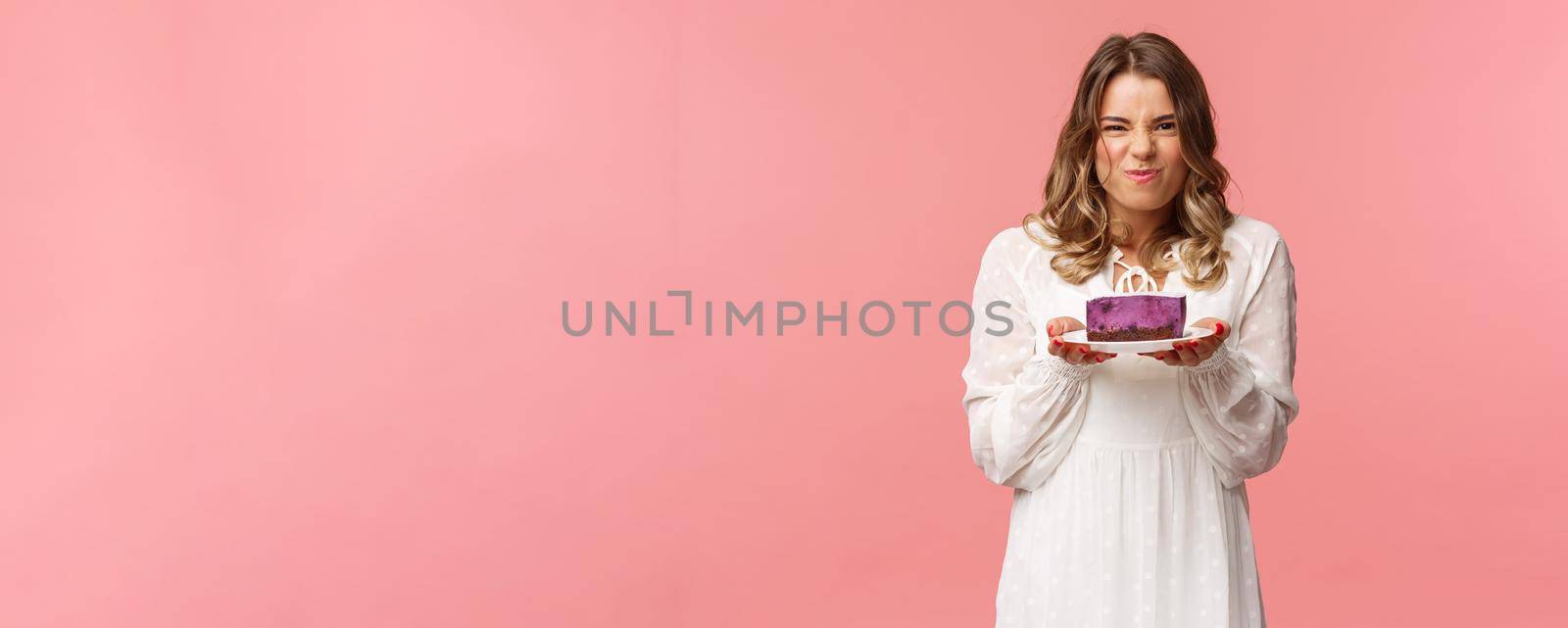 Holidays, spring and party concept. Portrait of excited and pleased blond female in white dress, holding piece of delicious cake and grimacing satisfied, cant wait to have bite of tasty dessert by Benzoix