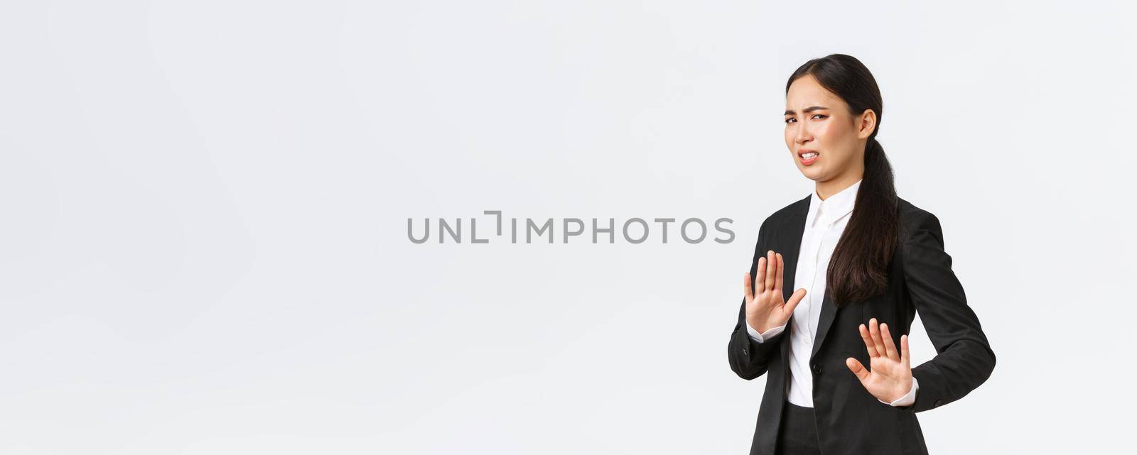 Displeased asian businesswoman avoiding risky suggestions, shaking hands in refusal, rejecting disgusting strange offer. Saleswoman grimacing from aversion and step away, white background.