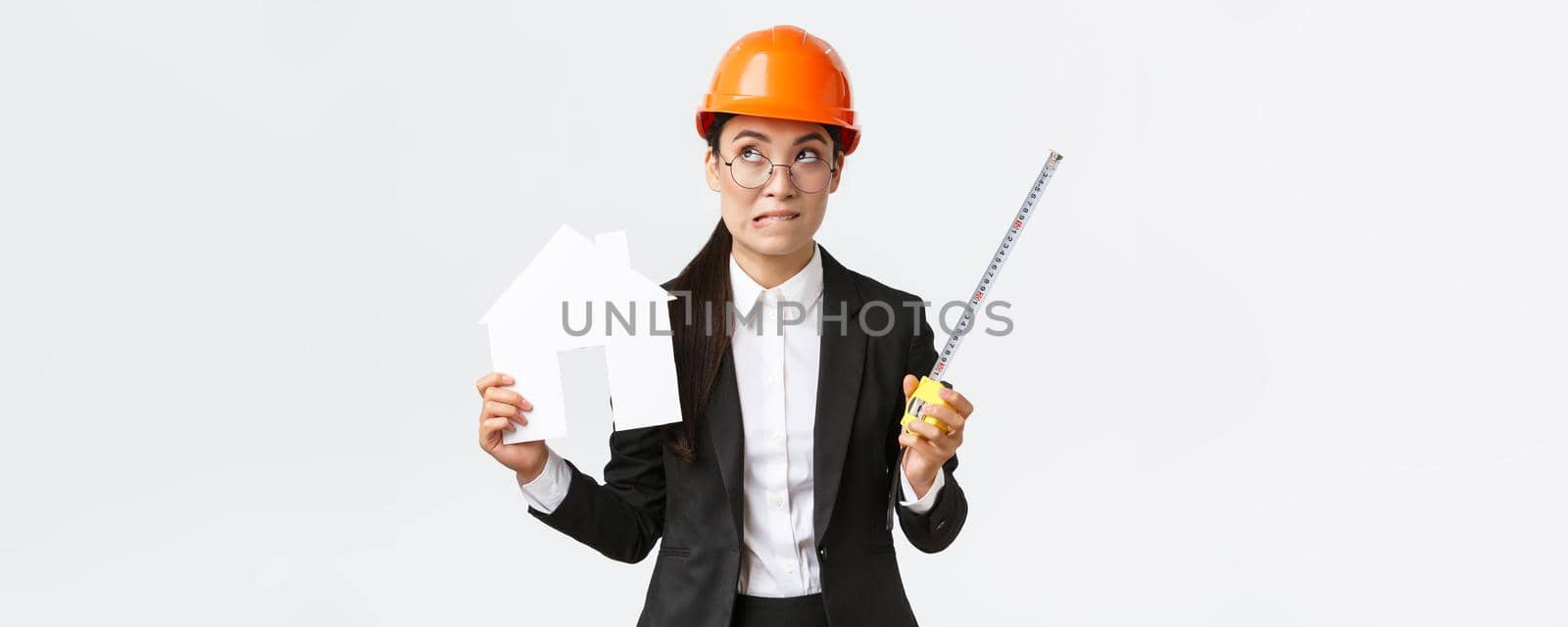 Indecisive asian female architect, construction engineer in helmet and business suit holding house maket and tape measure, biting lip unsure, looking away thoughtful, searching solution by Benzoix