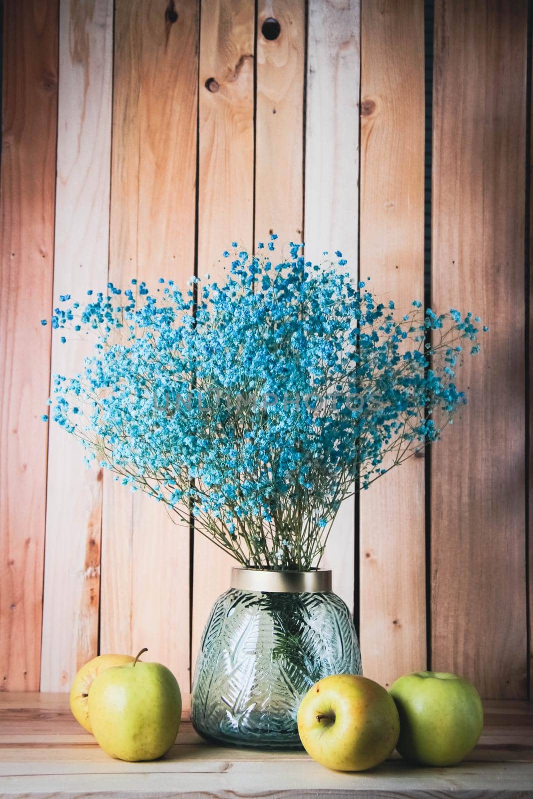 Vase with blue flowers and green apples on a wooden background. Still life in rustic style. Bouquet of gypsophila and fruits. Holiday decoration.