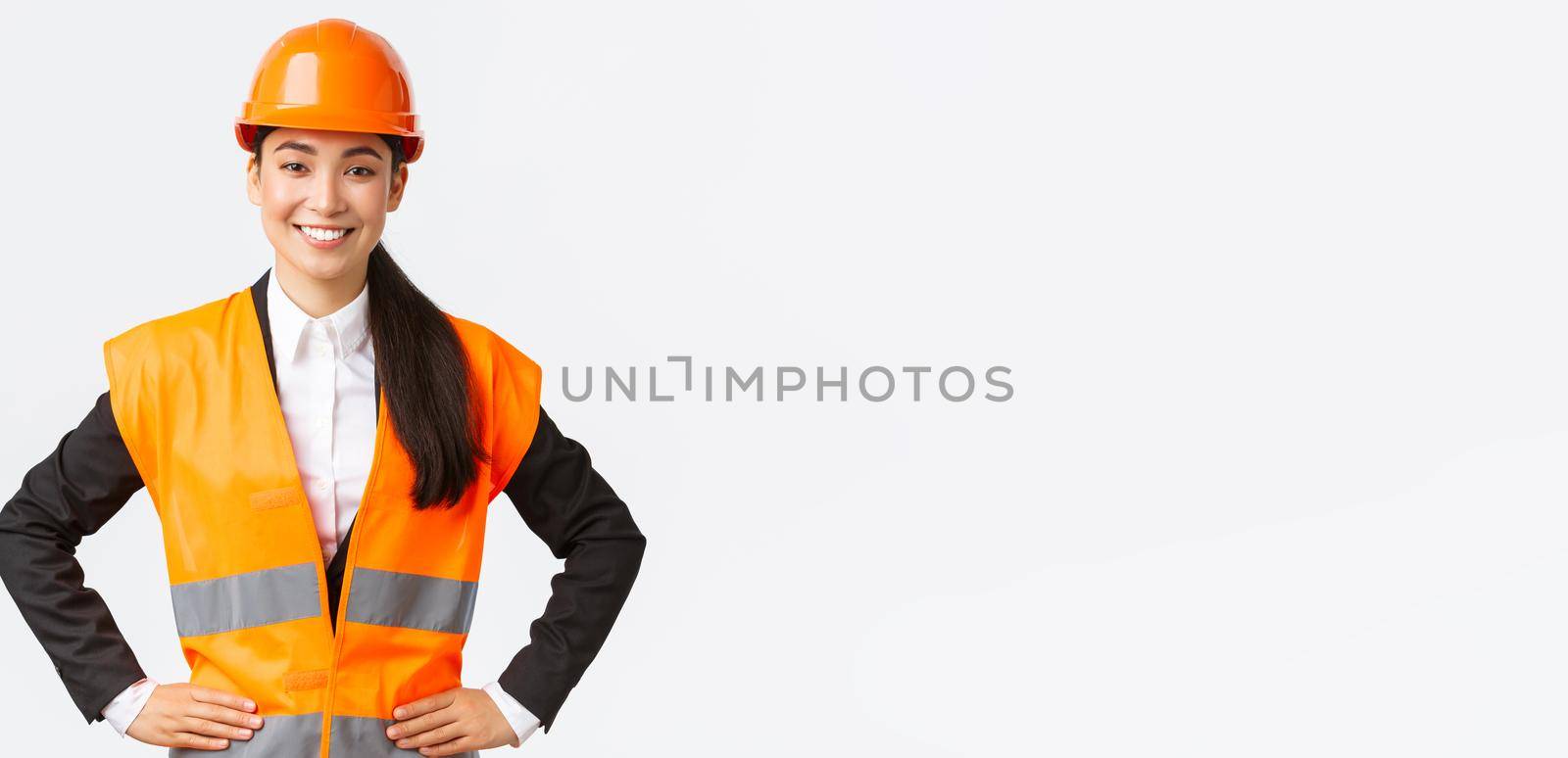 Successful young female asian businesswoman, architect in safety helmet, reflective jacket, standing confident and determined, smiling assured, building houses, posing over white background by Benzoix