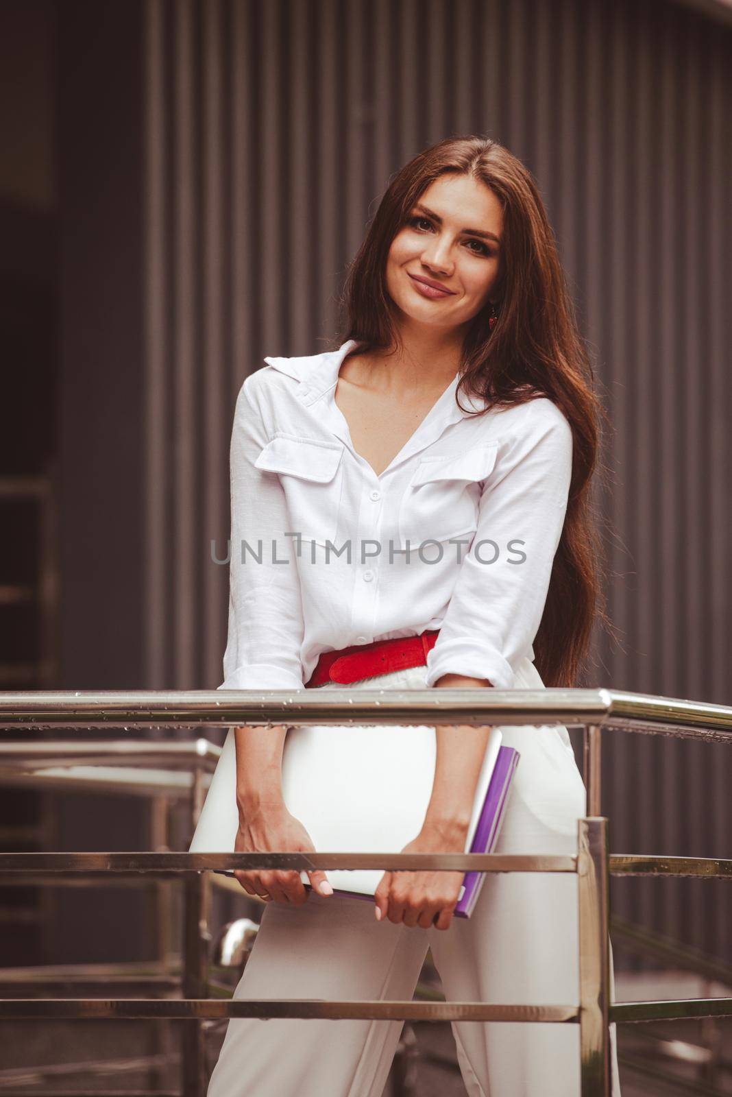 Beautiful young caucasian businesswoman in a white clothes with a laptop and notebook outdoor near business centre by Ashtray25