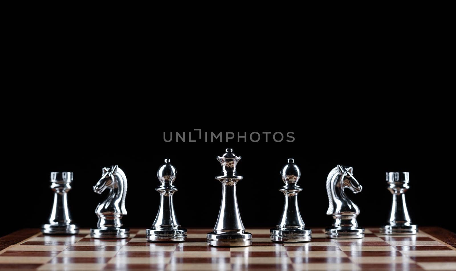 Silvery chess figures standing on chessboard. Intellectual competition and fight in business. Strategy planning and leadership concept with copy space. Silver chess pieces in row on black background.