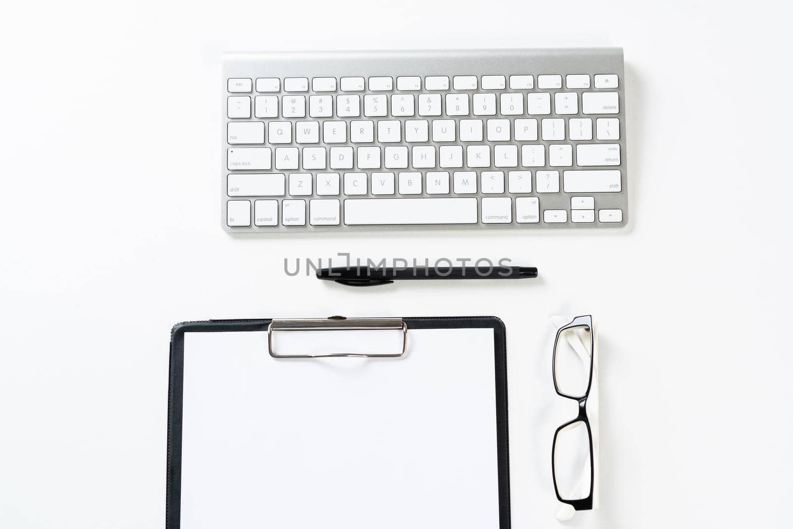 Top view of well organized workplace with office accessories. Clipboard with blank paper page, glasses and wireless keyboard on white surface. Education, creativity and working concept with copy space