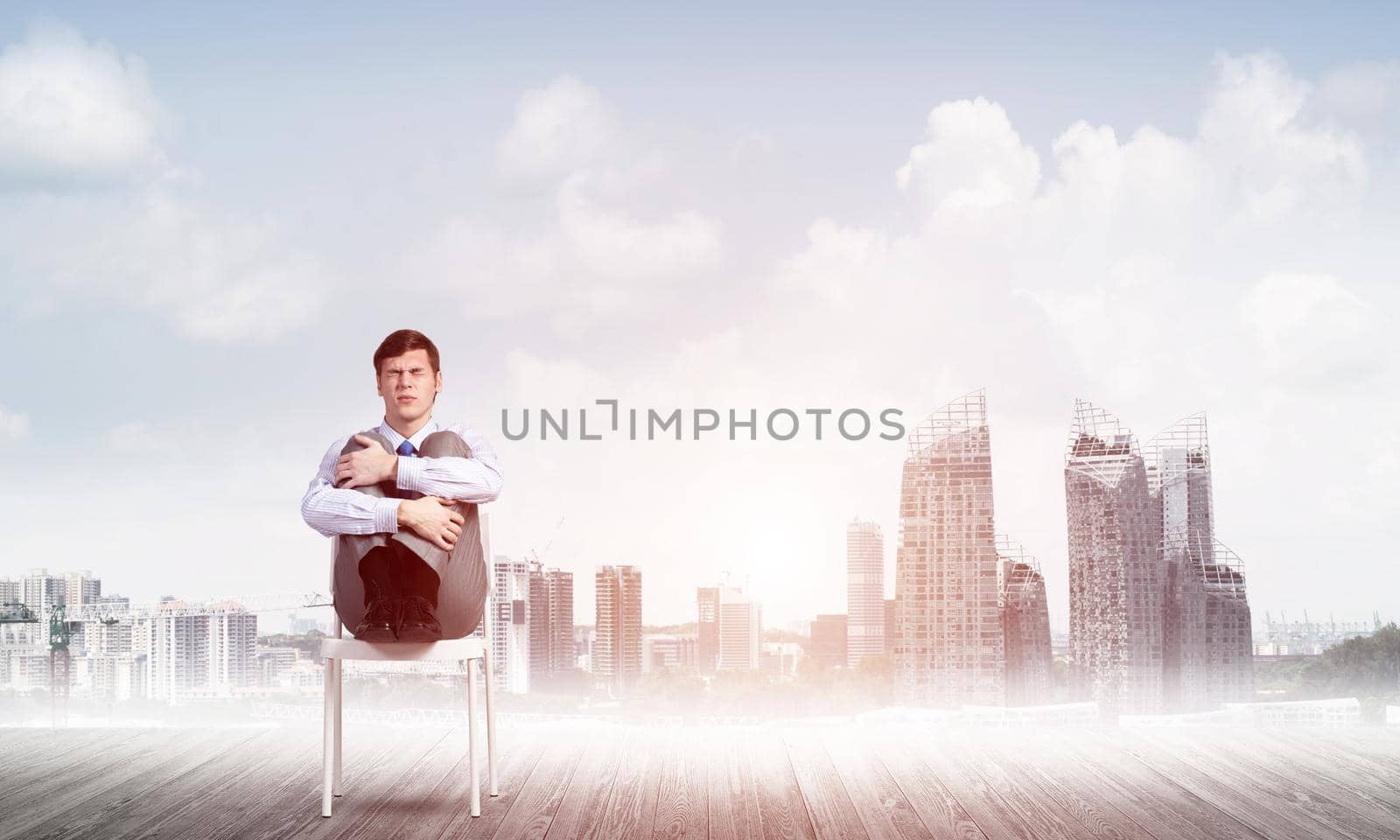 scared businessman sitting on a chair with his hands clasped his knees