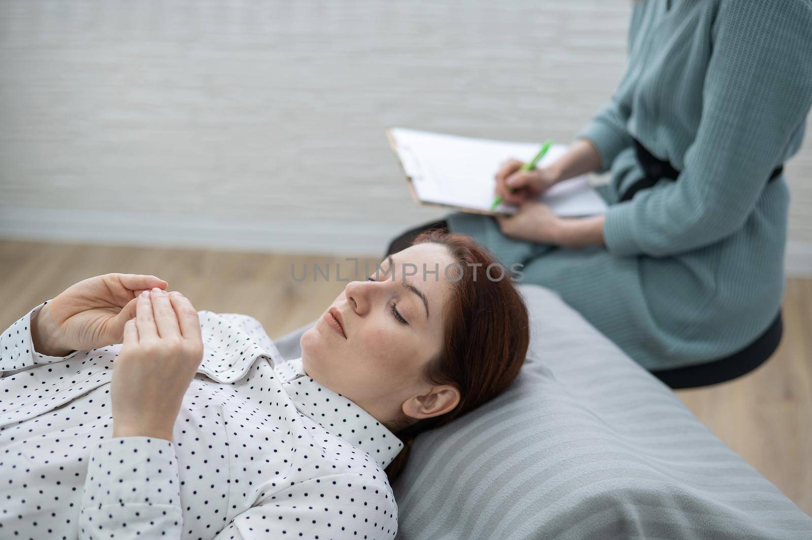 A caucasian woman lies on a couch and expresses her feelings, while a psychologist makes notes on a tablet. by mrwed54