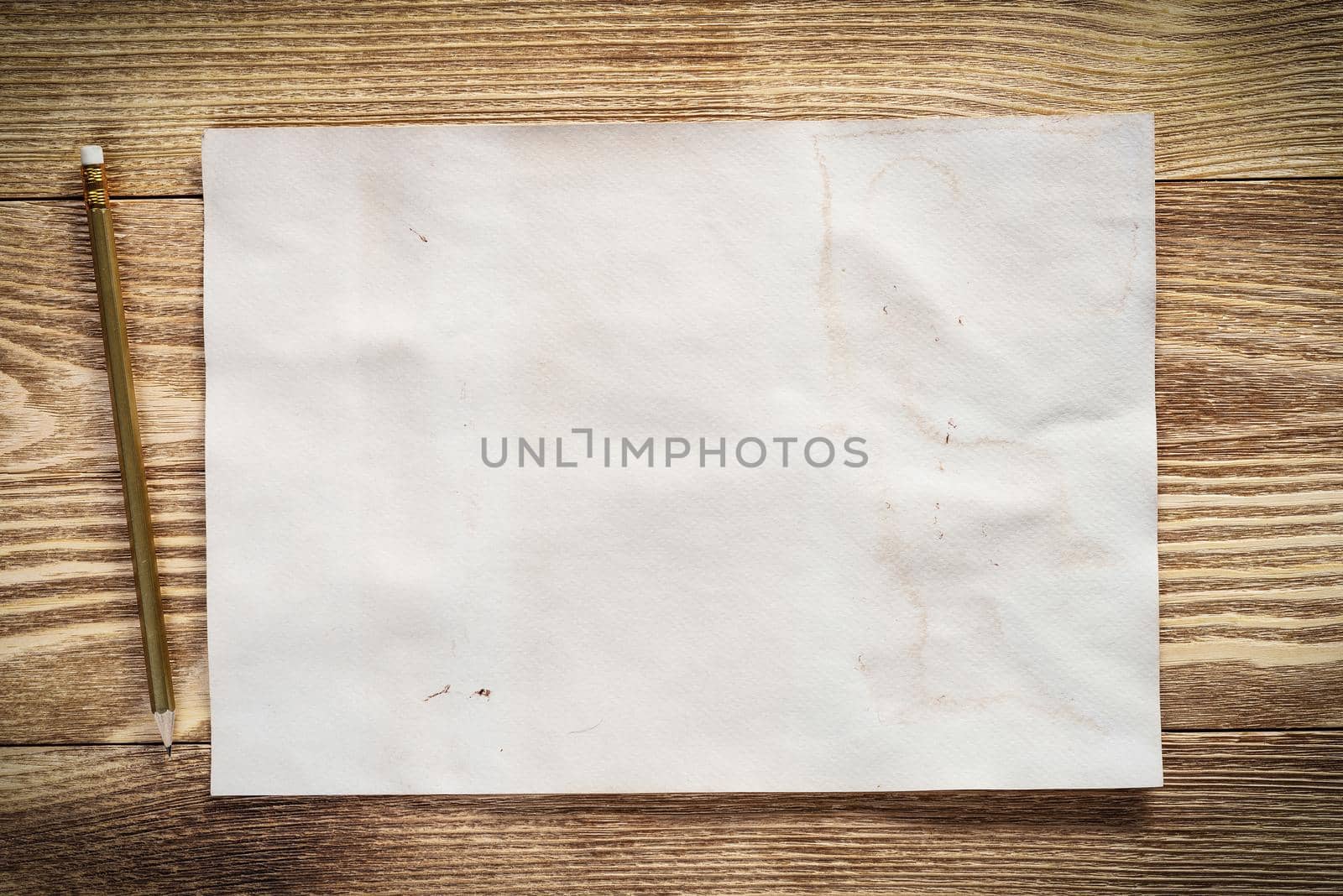 Sheet of paper lying on wooden table. Scrapbooking and hand made creativity. Rectangular blank white paper with pencil. Textured natural wooden background. View from above with copy space.