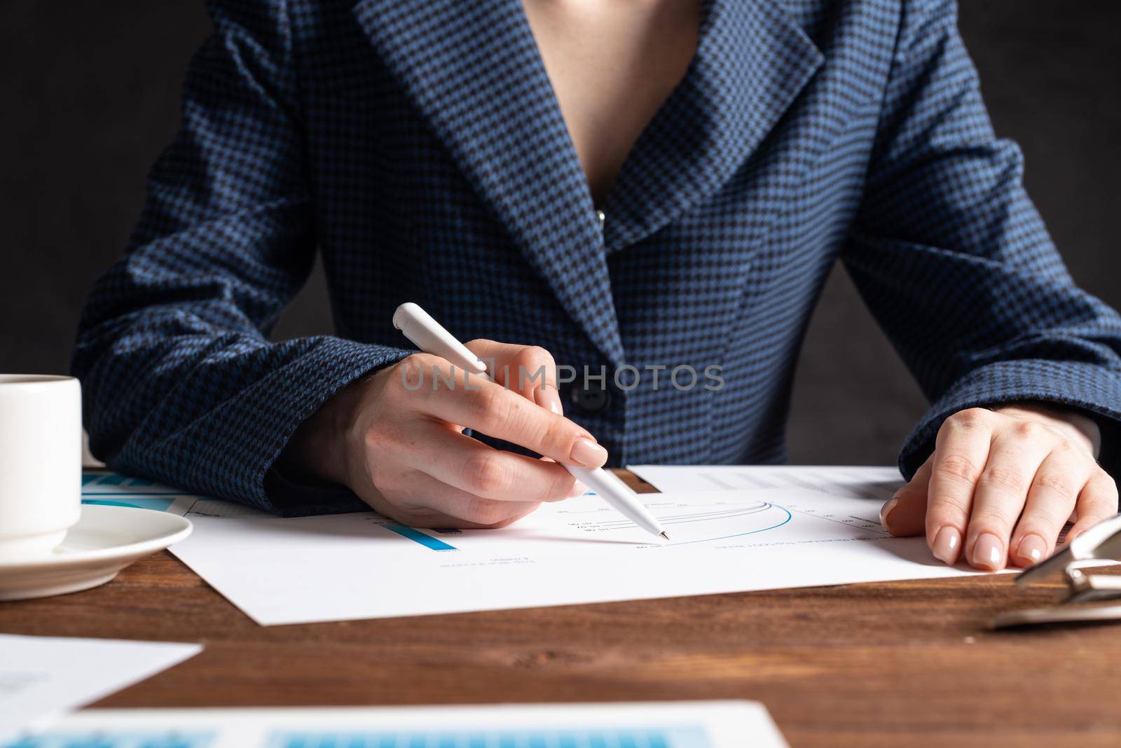 Corporate consultant analyze financial diagram. Close up woman hand with pen and coffee cup on wooden desk. Analyst in suit working at workplace in office. Business accounting and management.