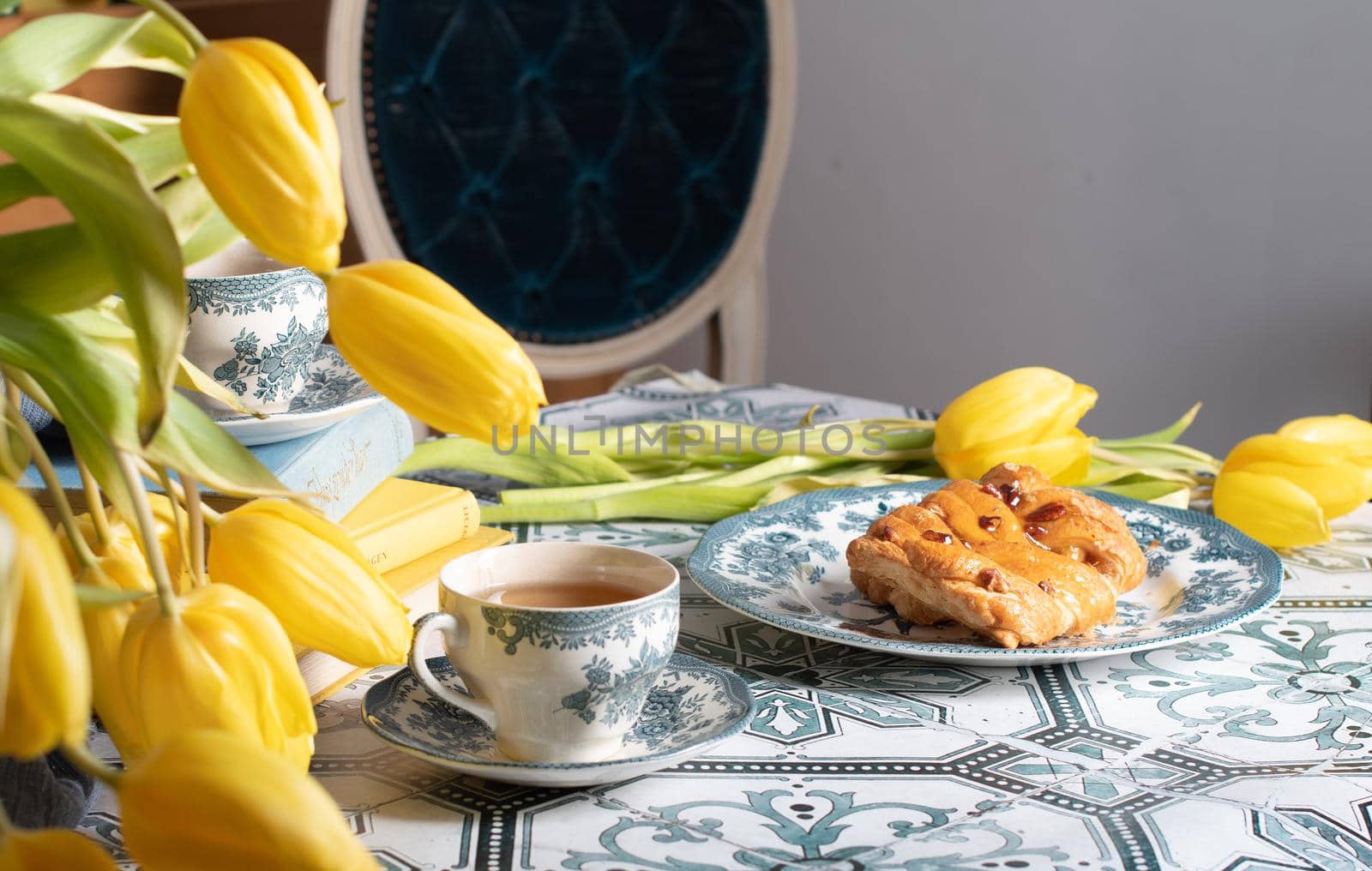 retro still life, sweet puff, tea in a vintage porcelain cup and a stack of books, a bouquet of yellow withering tulips in a vase,. High quality photo