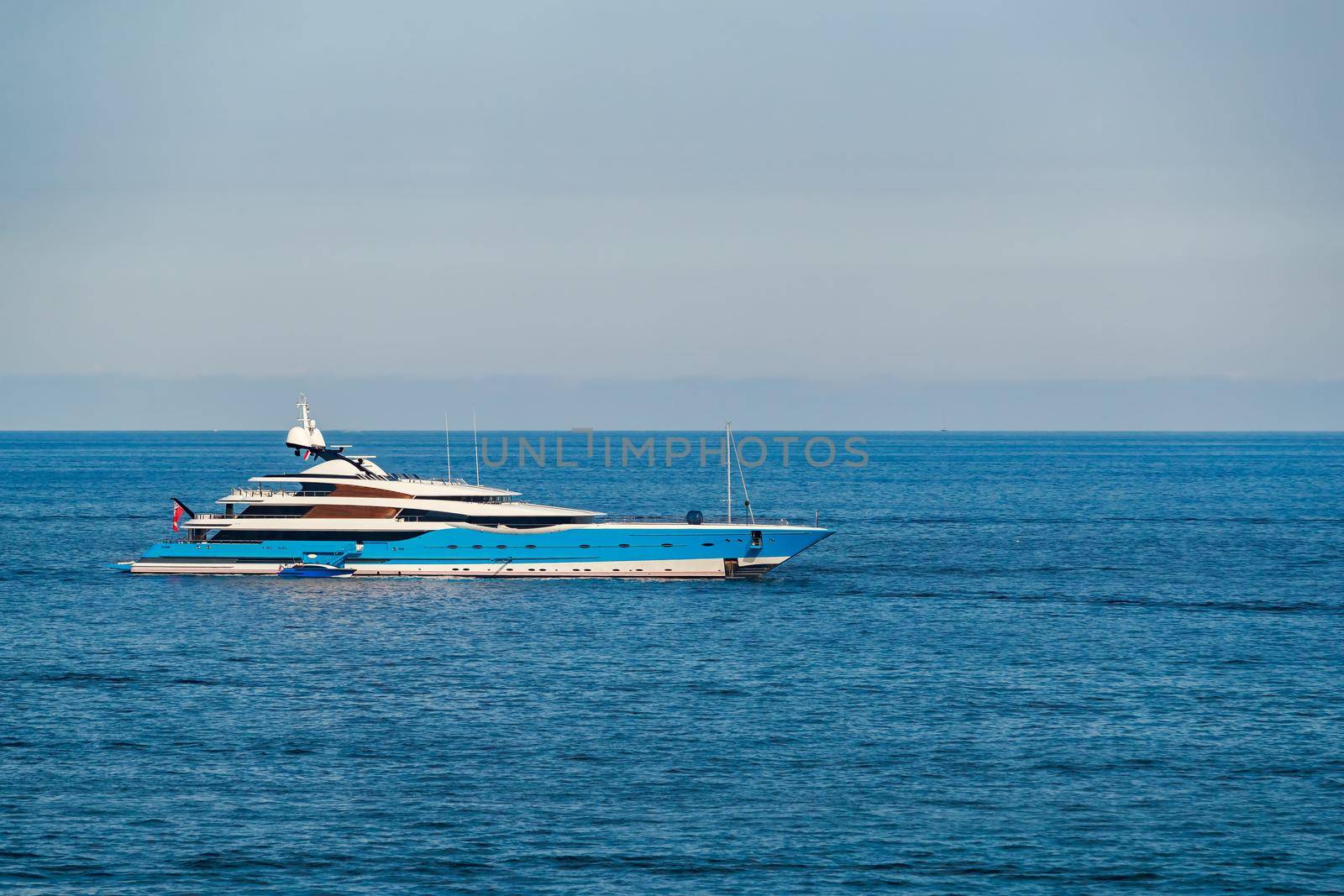 The huge mega yacht is moored in sea off the coast of the azur coastline at sunny day, the chrome plated handrail, sun reflection on glossy board of the motor boat. High quality photo