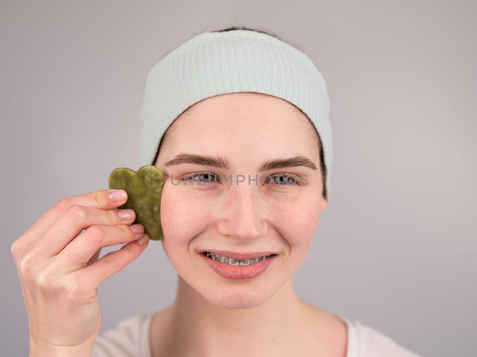 Close-up portrait of a smiling woman with braces doing home care with a gouache massager