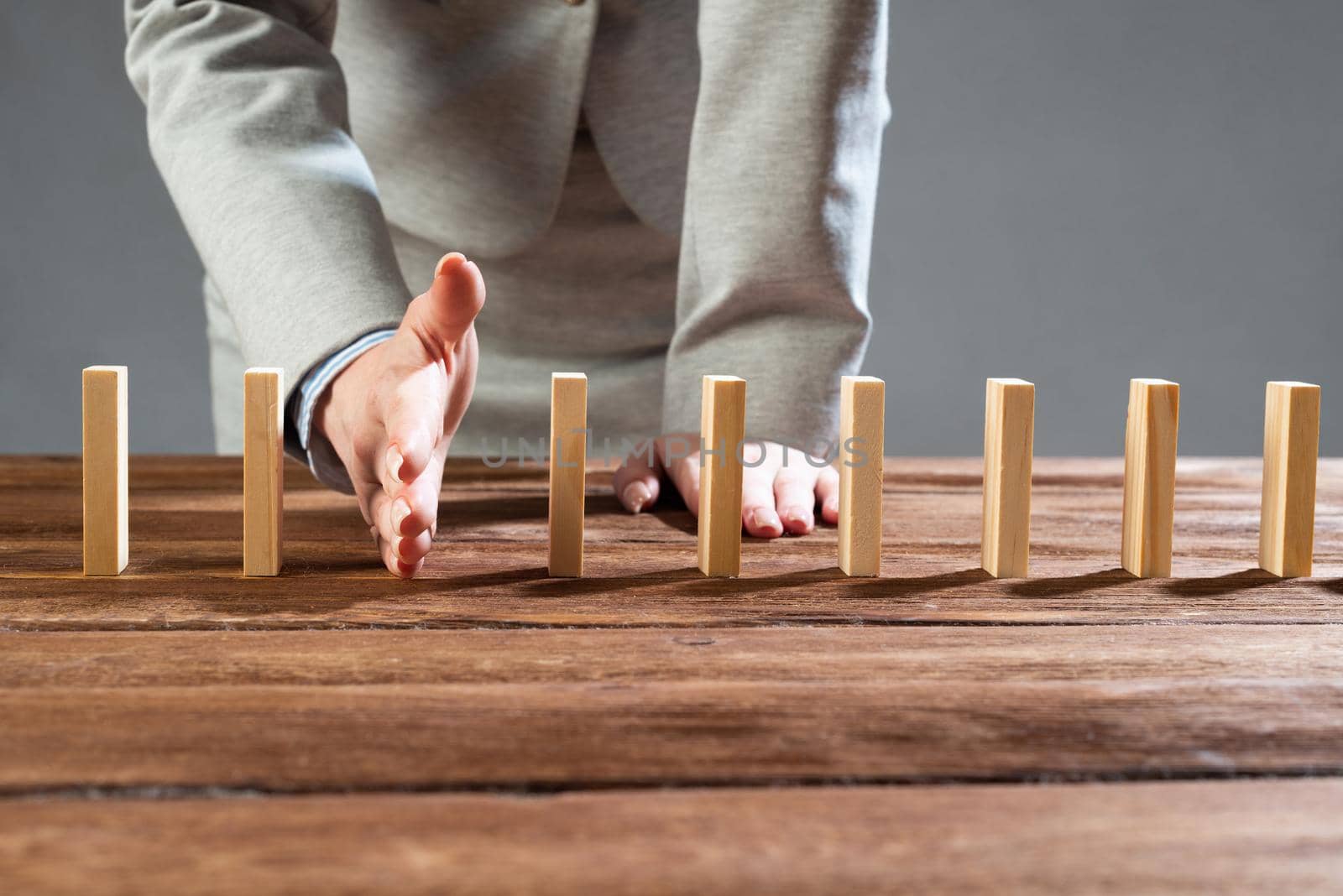 Businesswoman protecting dominoes from falling on wooden desk. Business assistance and leadership in crisis. Operative business solution and stabilization of situation. Professional risk management