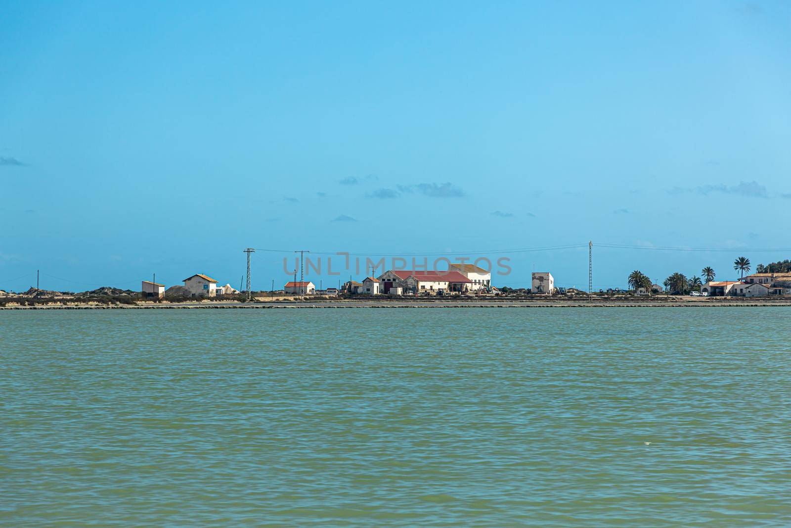Some buildings on the shore of a salt lake. Blue sky and green water.