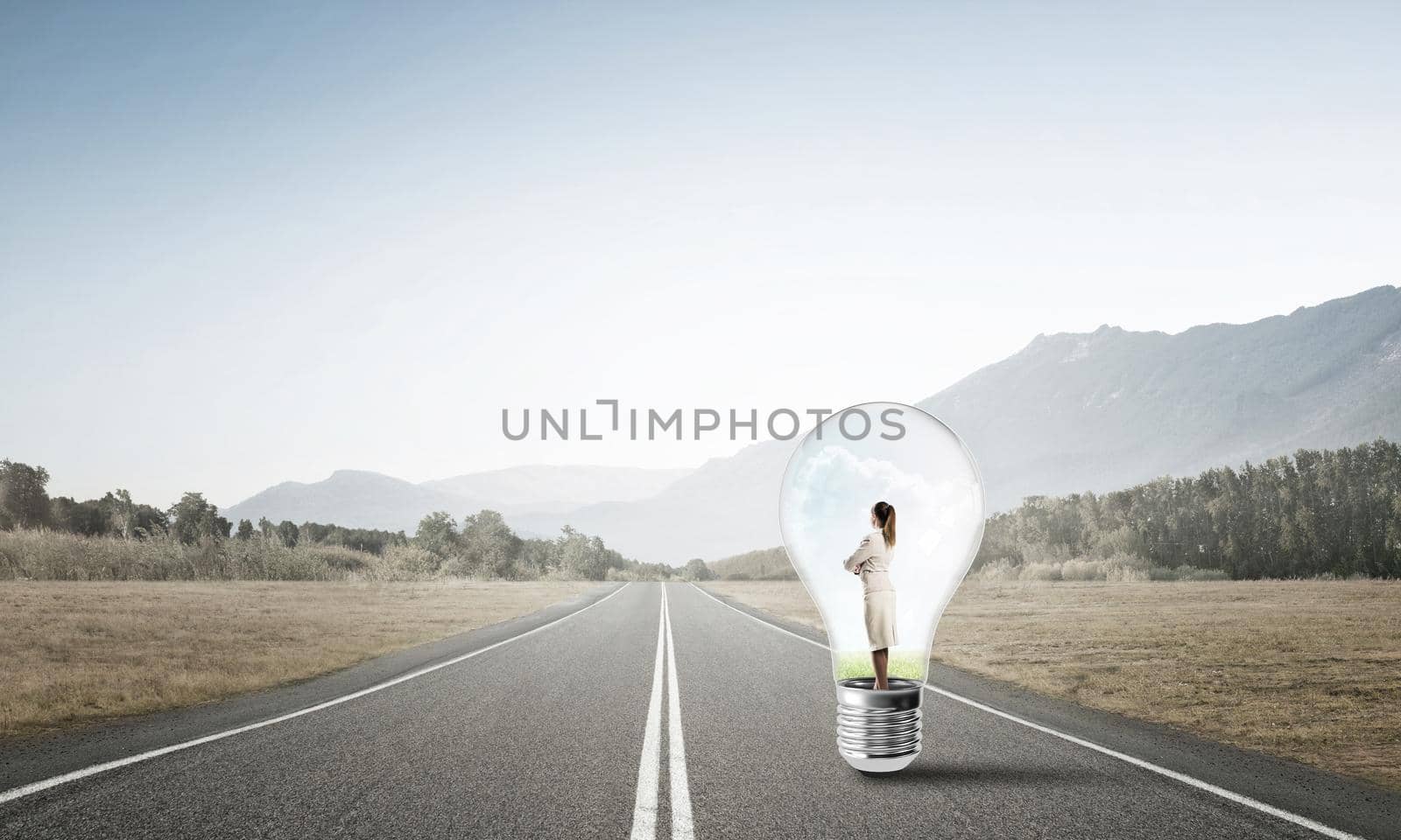 Young businesswoman trapped inside of light bulb on asphalt road