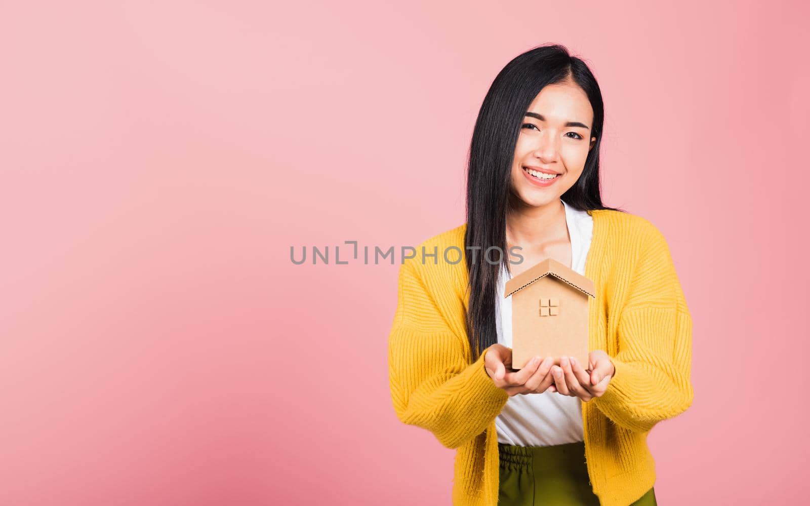 Happy Asian portrait beautiful cute young woman excited smiling holding house model on hand, studio shot isolated on pink background, broker female hold home real estate insurance and banking concept