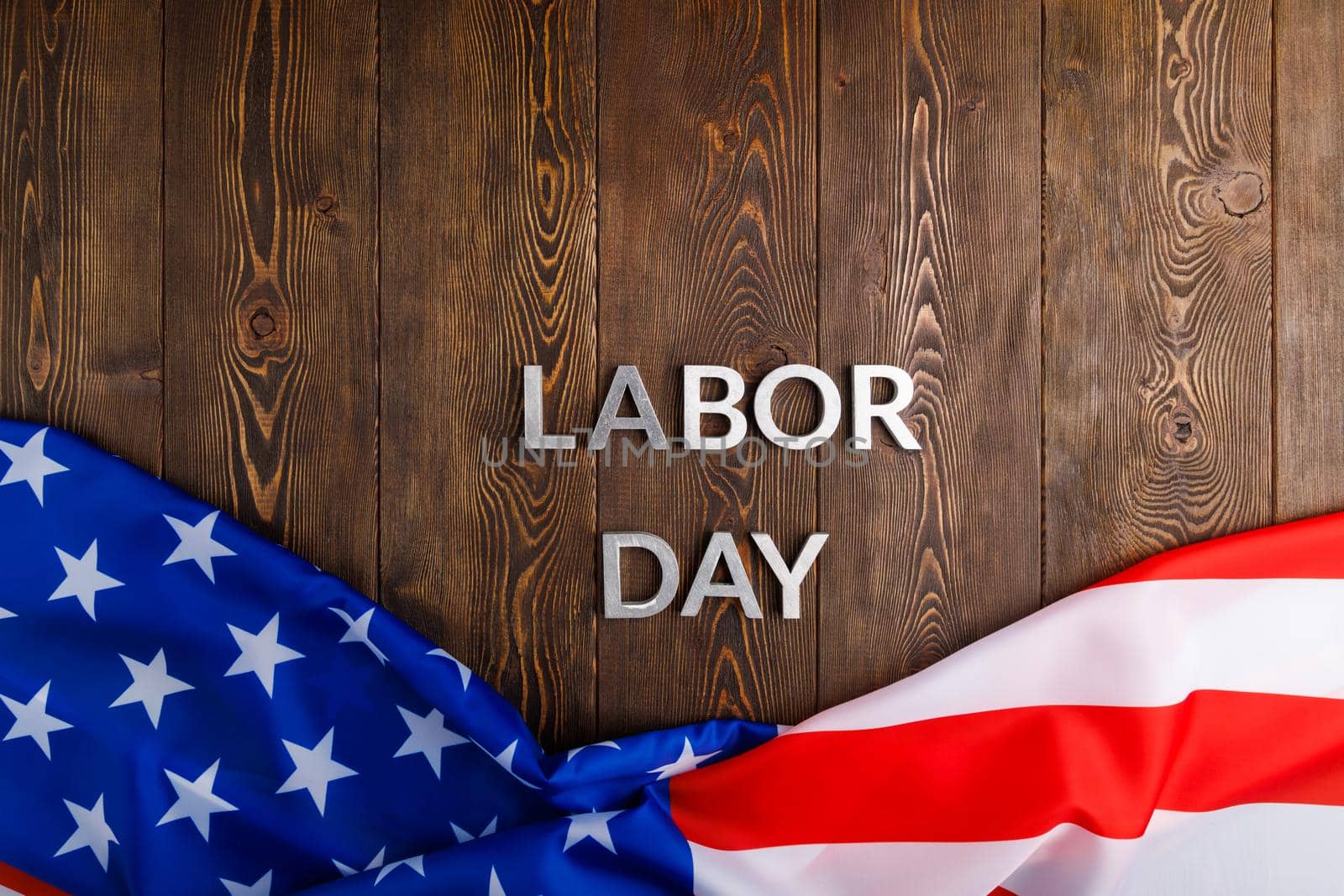 words labor day laid with silver metal letters on wooden surface with crumpled USA flag on bottom side in directly above high angle view