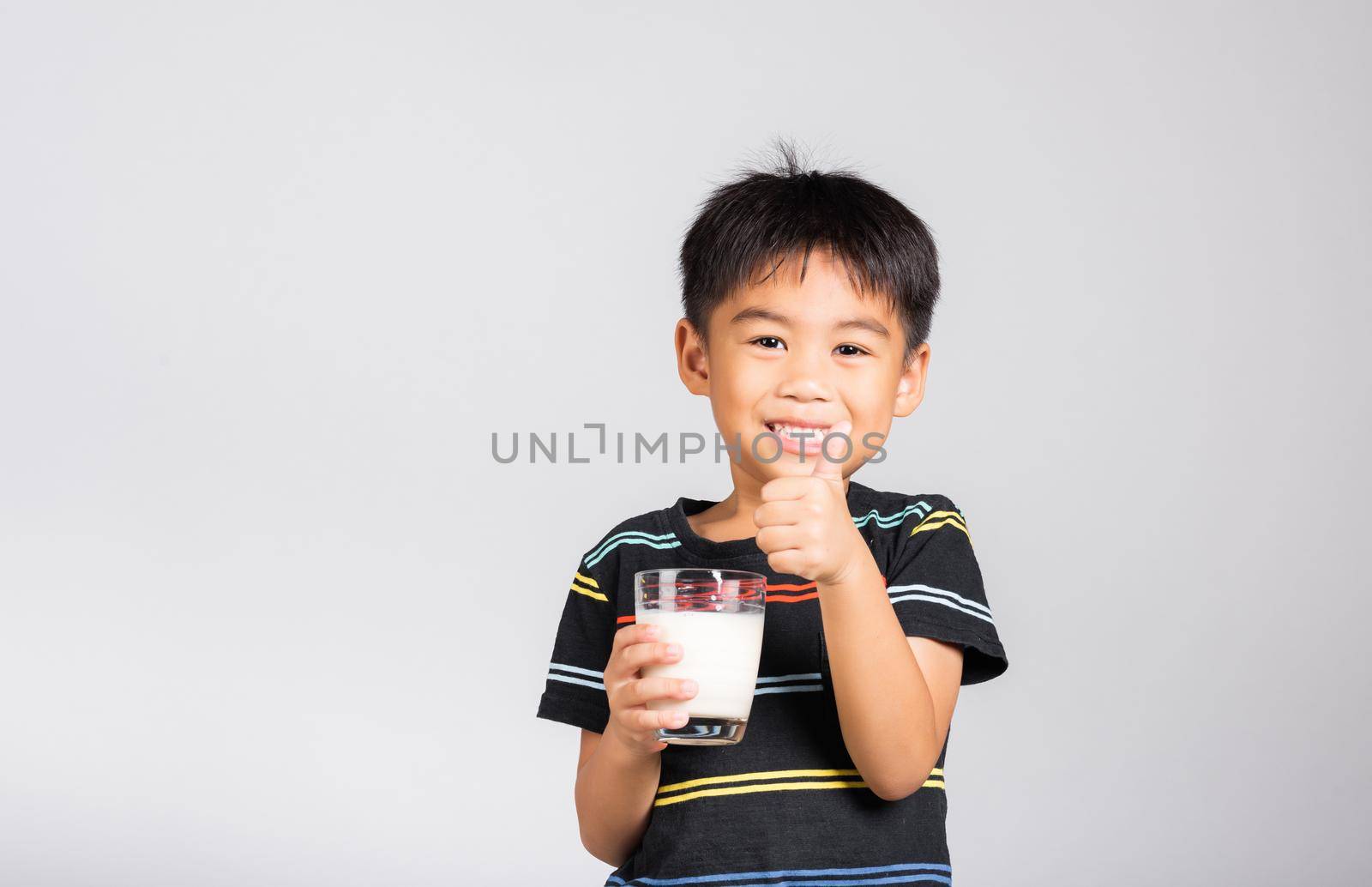 Little kid boy 5-6 years old smile holding milk glass he drinking white milk and show thumb up finger for good sign by Sorapop