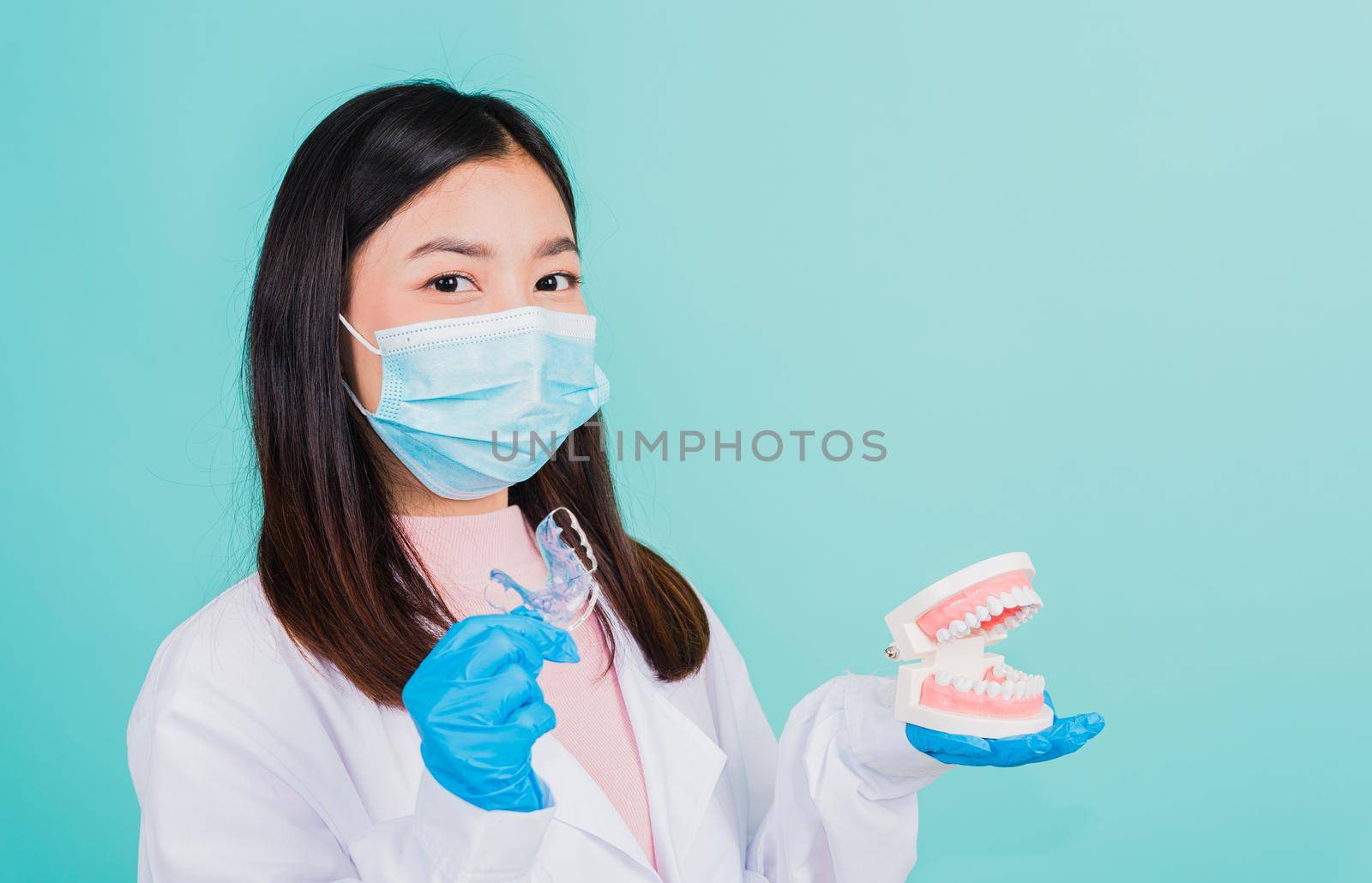 Asian beautiful woman dentist holding silicone orthodontic retainers and model teeth denture isolated on blue background, Teeth retaining tools after removable braces, Orthodontics dental healthy care