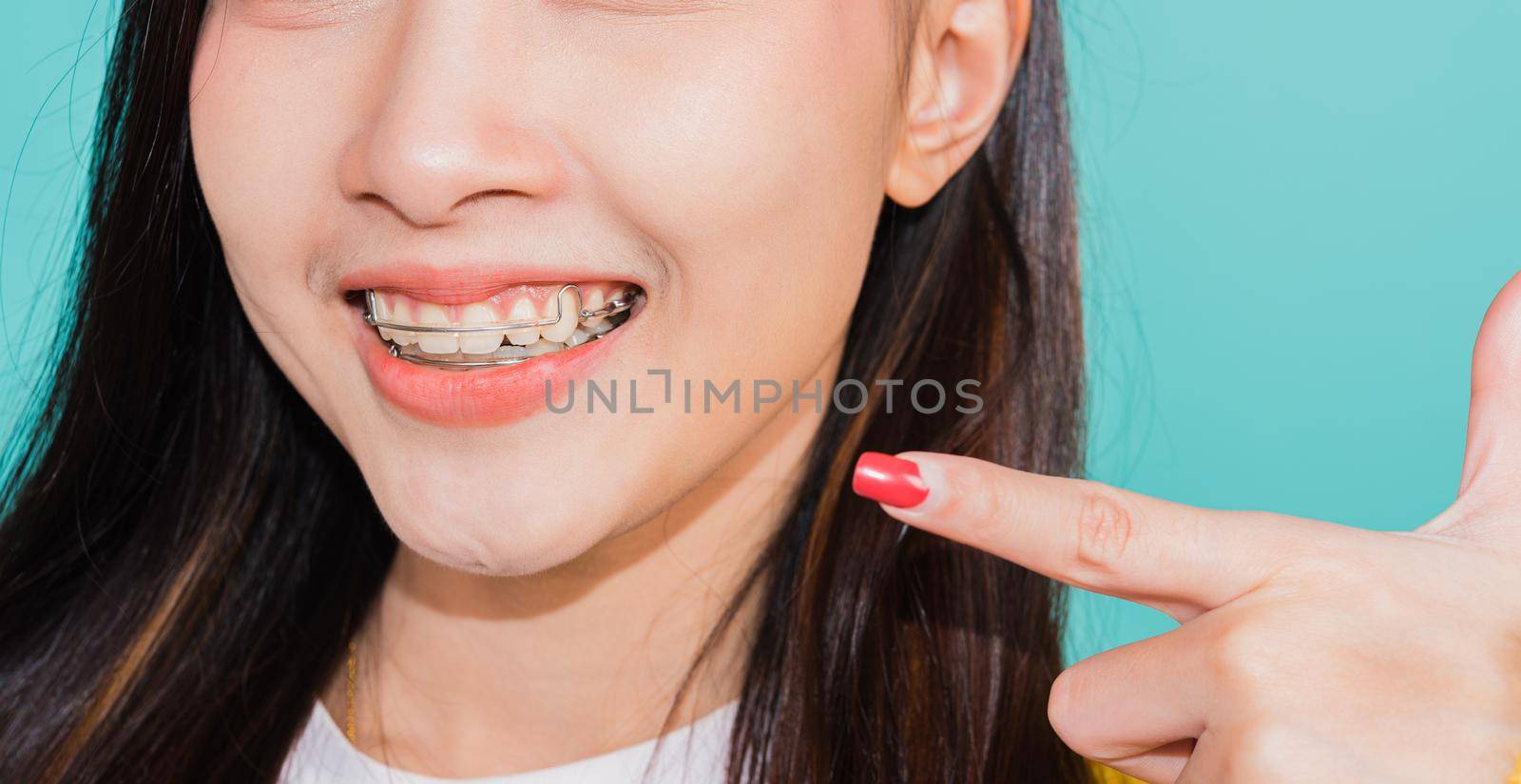 Asian beautiful young woman teen pointing finger to teeth, portrait of happy Thai female confident smiling show white teeth, studio shot isolated on blue background, Dental health care concept