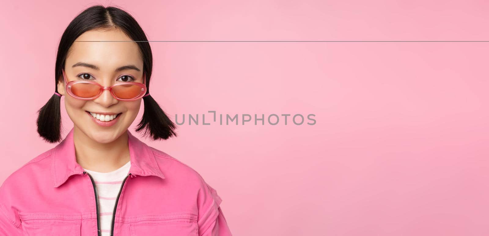 Close up of stylish korean girl in sunglasses, smiling happy, posing against pink background. People face concept by Benzoix