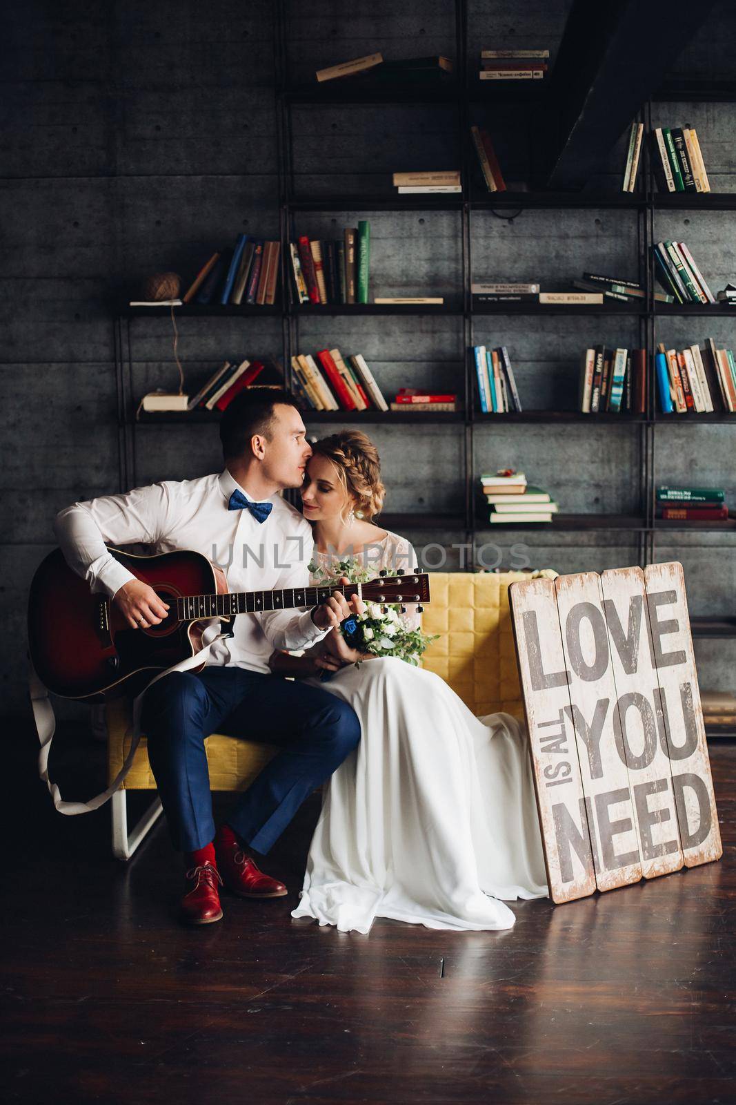 Beautiful smiling couple in red sweaters listening music, girlfriend leaning on handsome boyfriend, when he playing at gitar. Celebrating new year and xmas. Romantic winter holidays.