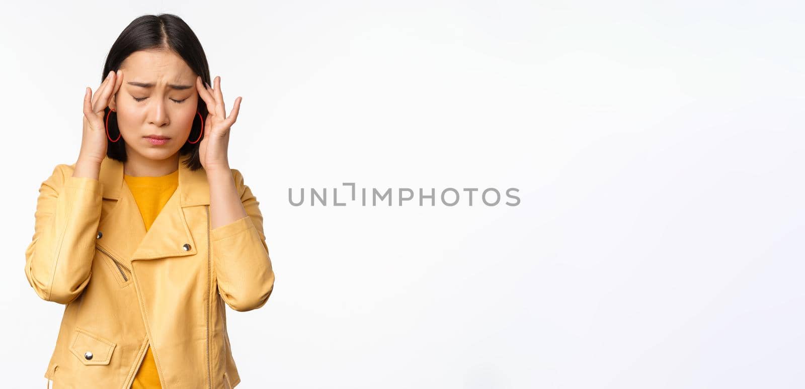 Image of asian woman massaging head temples with concerned face, suffering headache, migraine, standing over white background.