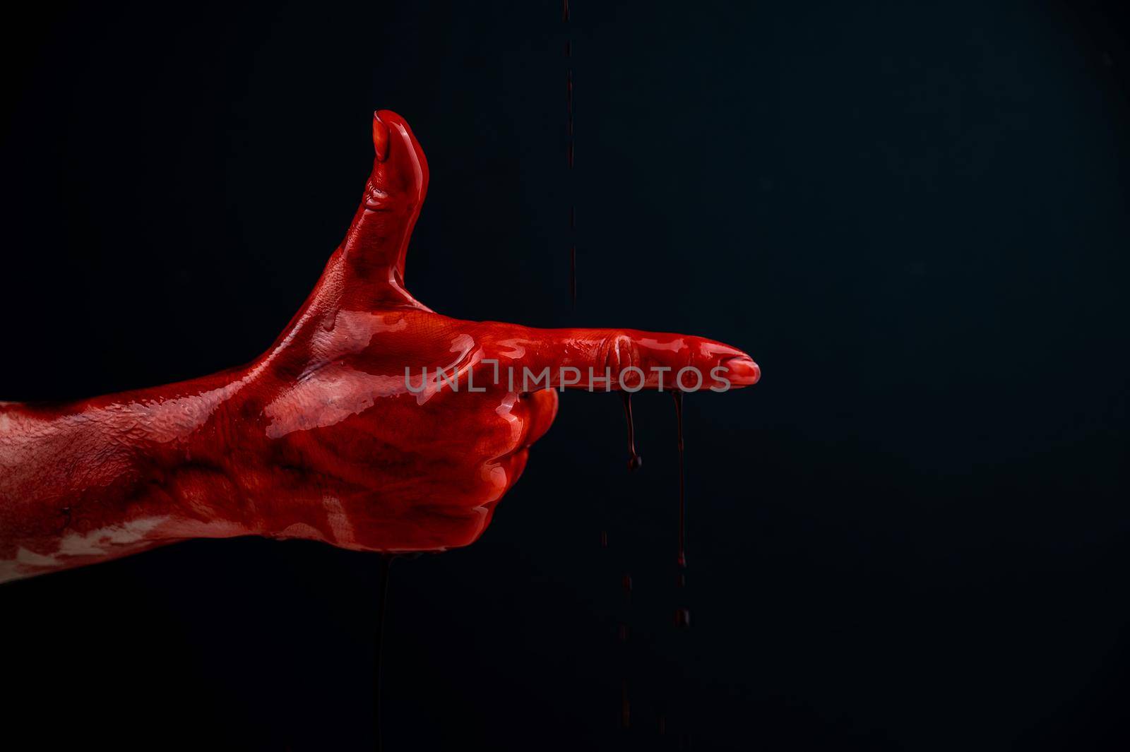 Woman's hand in blood shows a gesture of a gun on a black background