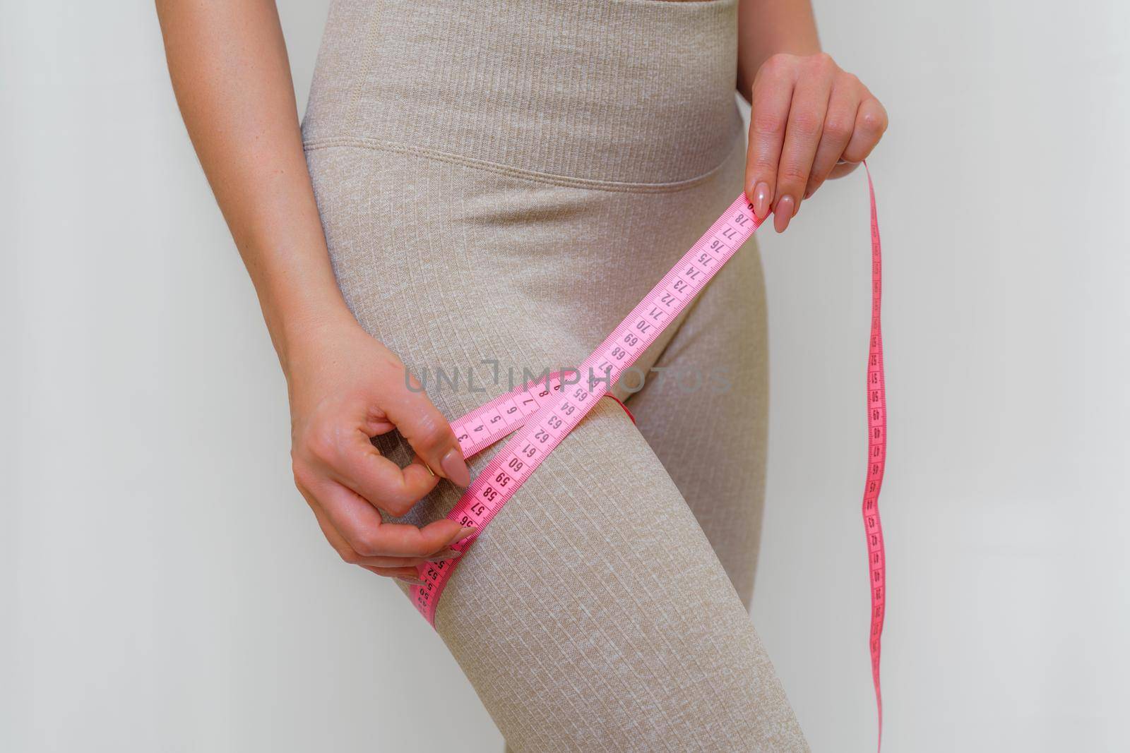 Cropped view of slim woman measuring her leg with tape measure at home, close-up. An unrecognizable European woman checks the result of a weight loss diet or liposuction indoors. Healthy lifestyle
