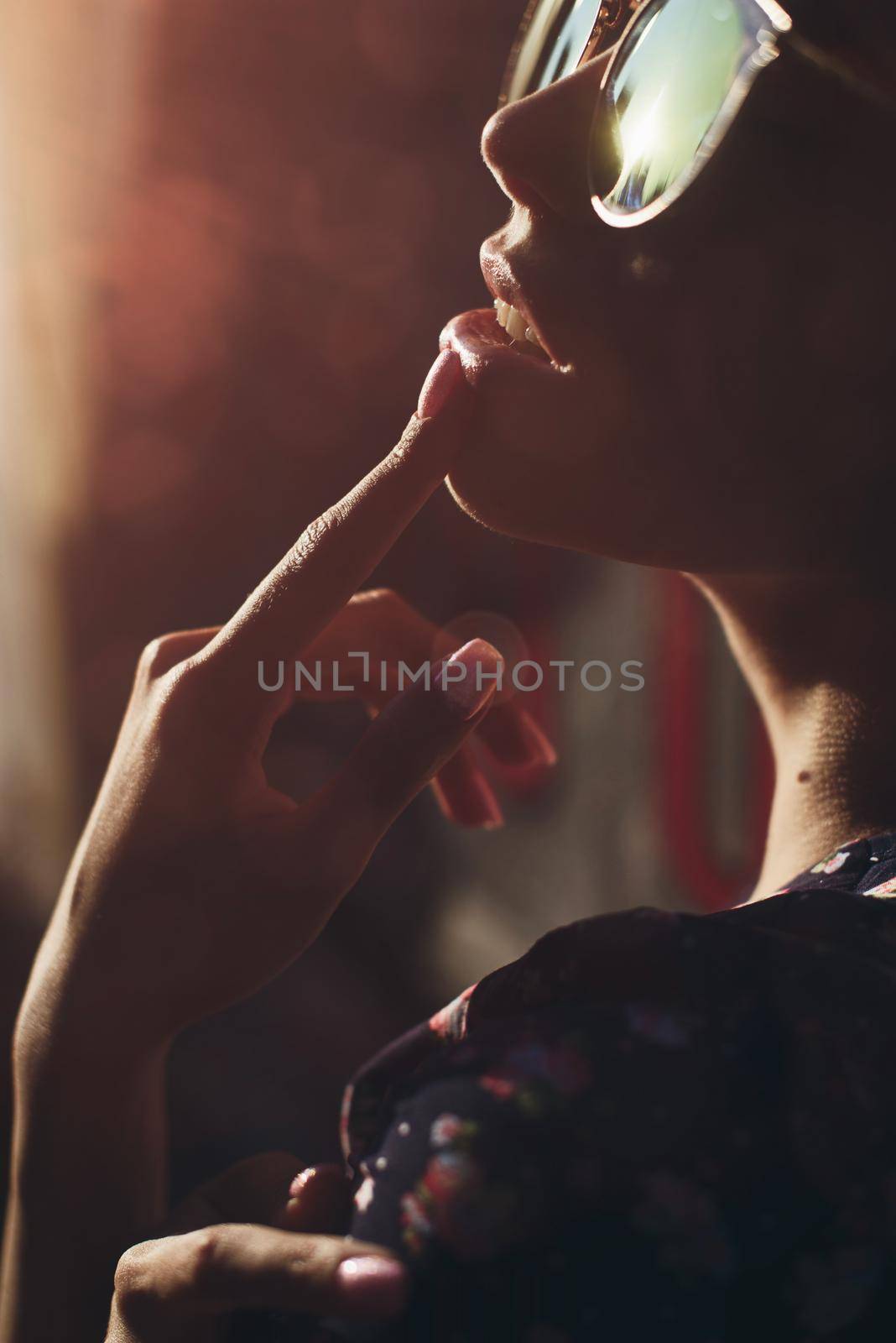 Close-up portrait of stylish young woman. Brunette in sundress posing on street. Finger near her lips