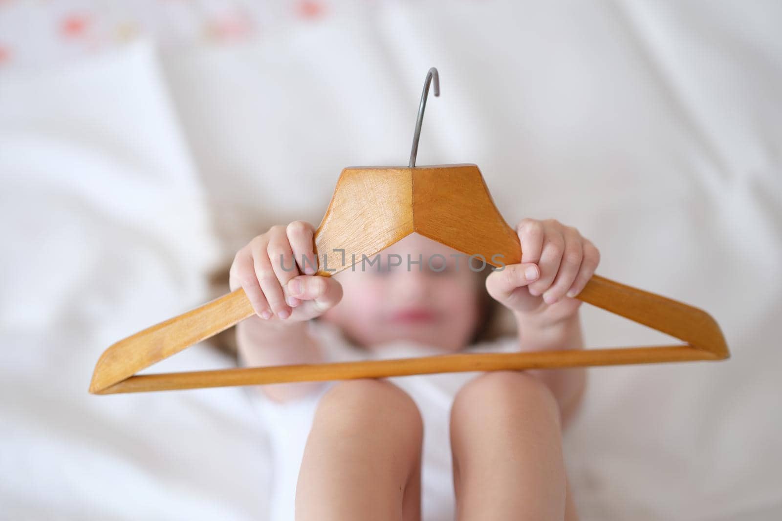 Child girl holding wooden hanger. Arrival at hotel concept