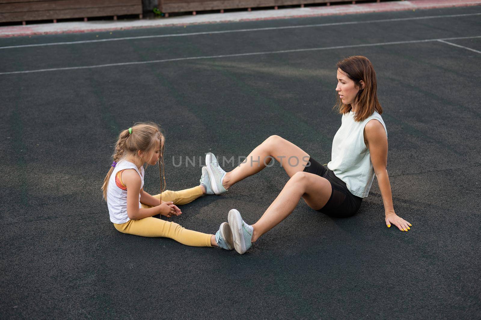 Mother and daughter go in for sports outdoors. Caucasian woman and little girl are engaged in fitness at the stadium. by mrwed54