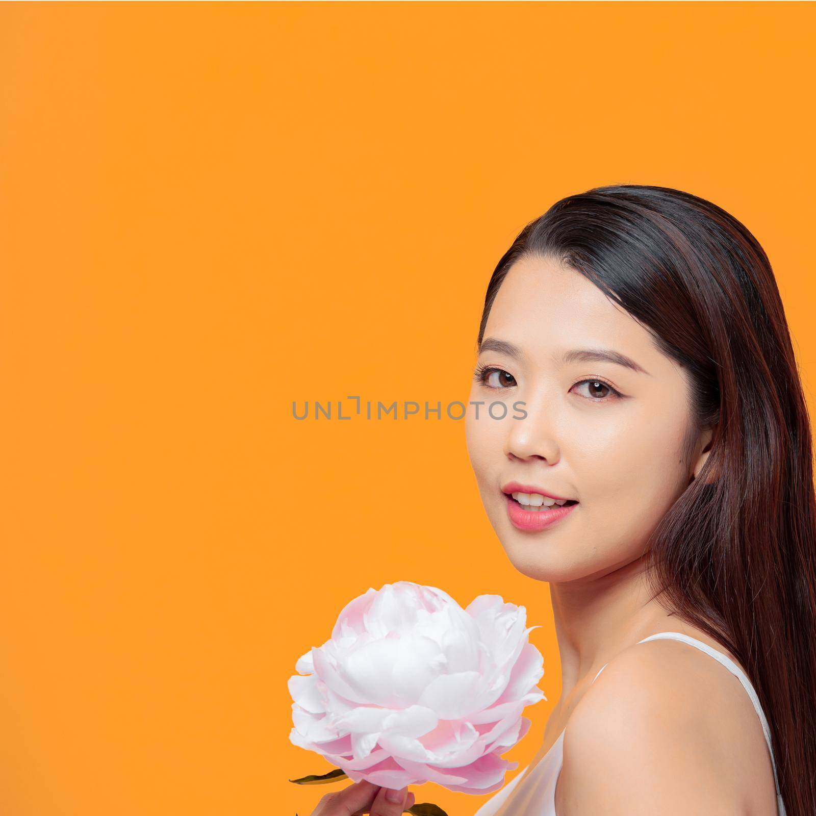 Adorable young woman holding pink peony flower in hands isolated over yellow by makidotvn